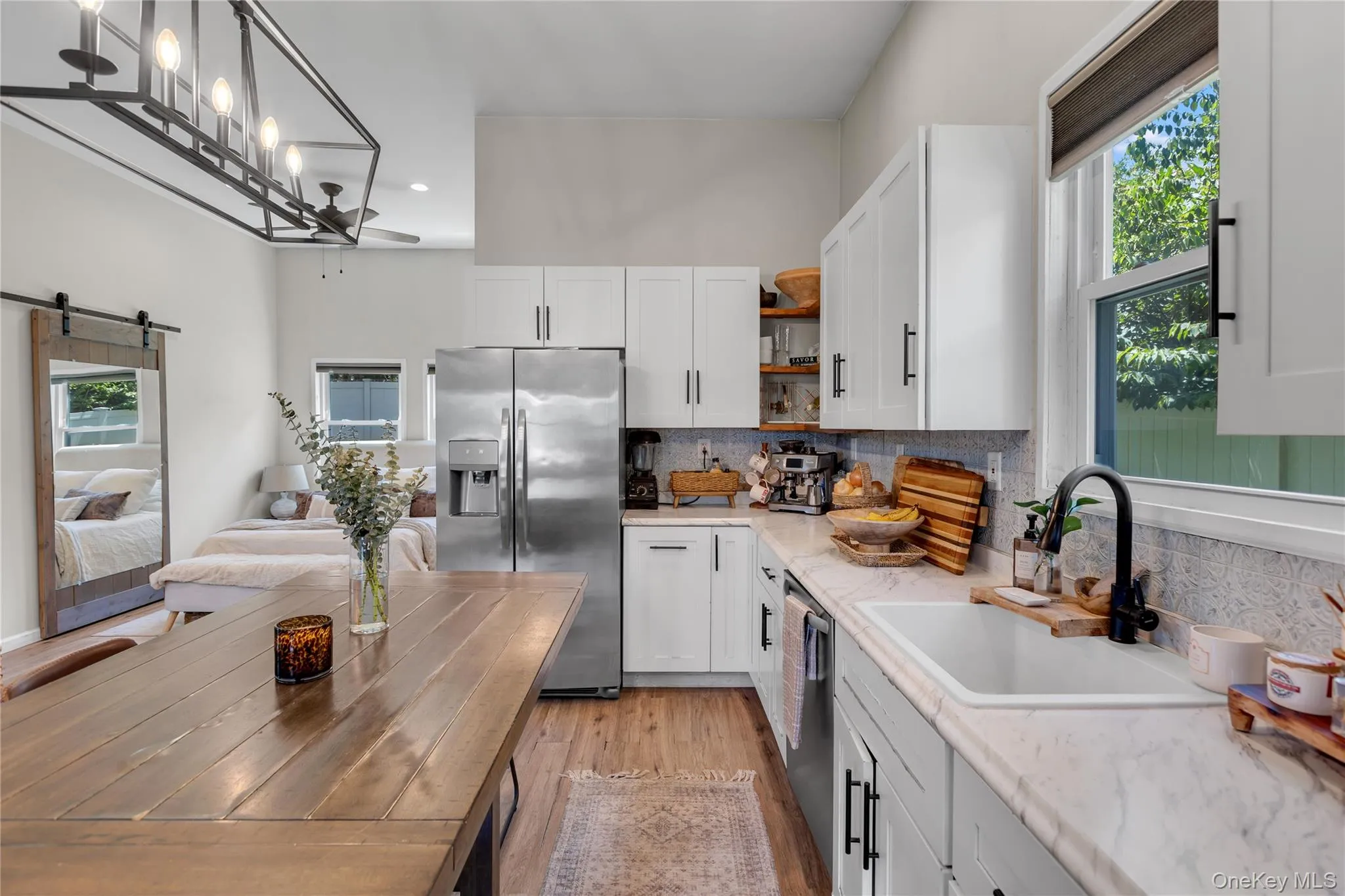 Modern kitchen featuring white shaker cabinetry, stainless steel appliances, a farmhouse sink with a matte black faucet, and patterned tile backsplash Modern kitchen featuring white shaker cabinetry, stainless steel appliances, a farmhouse sink with a matte black faucet, and patterned tile backsplash