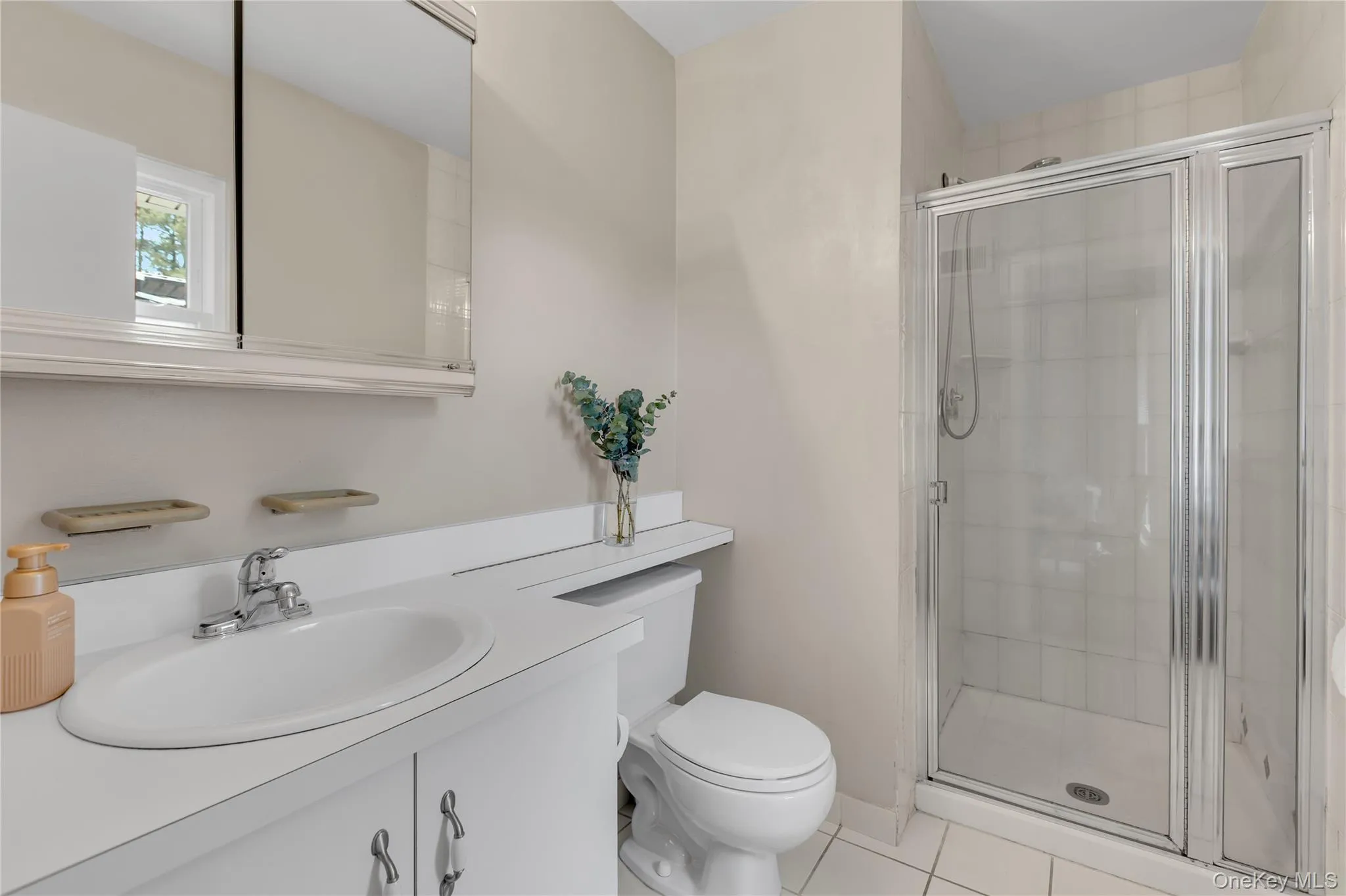 Bathroom featuring a glass-enclosed shower, white tile flooring, a single vanity with a white countertop, and a mirrored medicine cabinet Bathroom featuring a glass-enclosed shower, white tile flooring, a single vanity with a white countertop, and a mirrored medicine cabinet