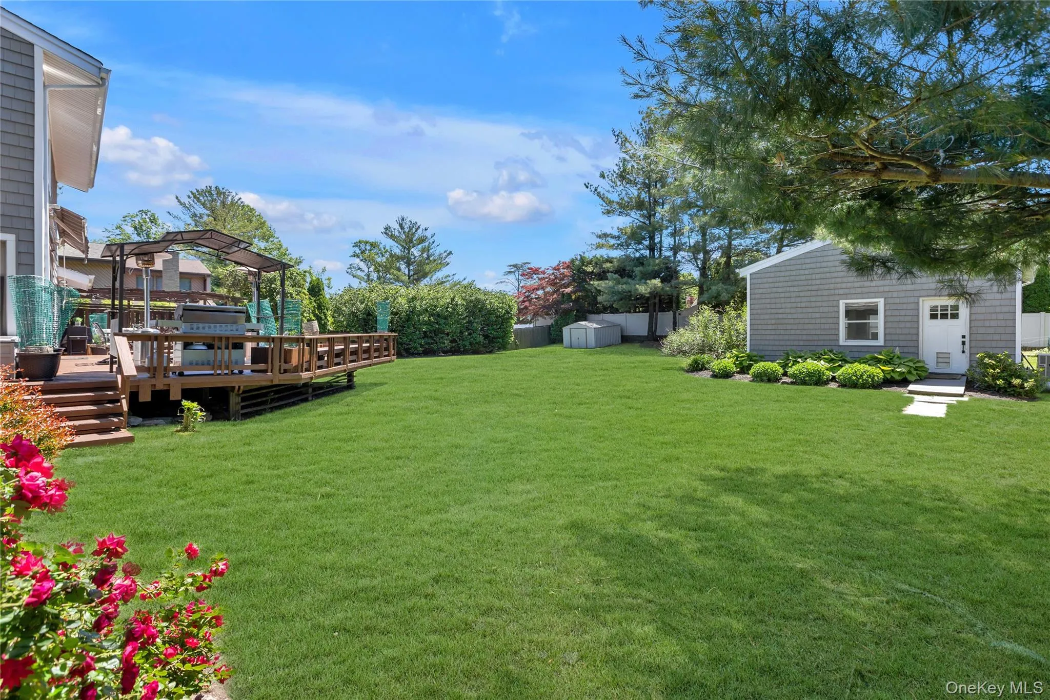 Expansive rear yard featuring a large wood deck, lush green lawn, and mature perimeter landscaping Expansive rear yard featuring a large wood deck, lush green lawn, and mature perimeter landscaping