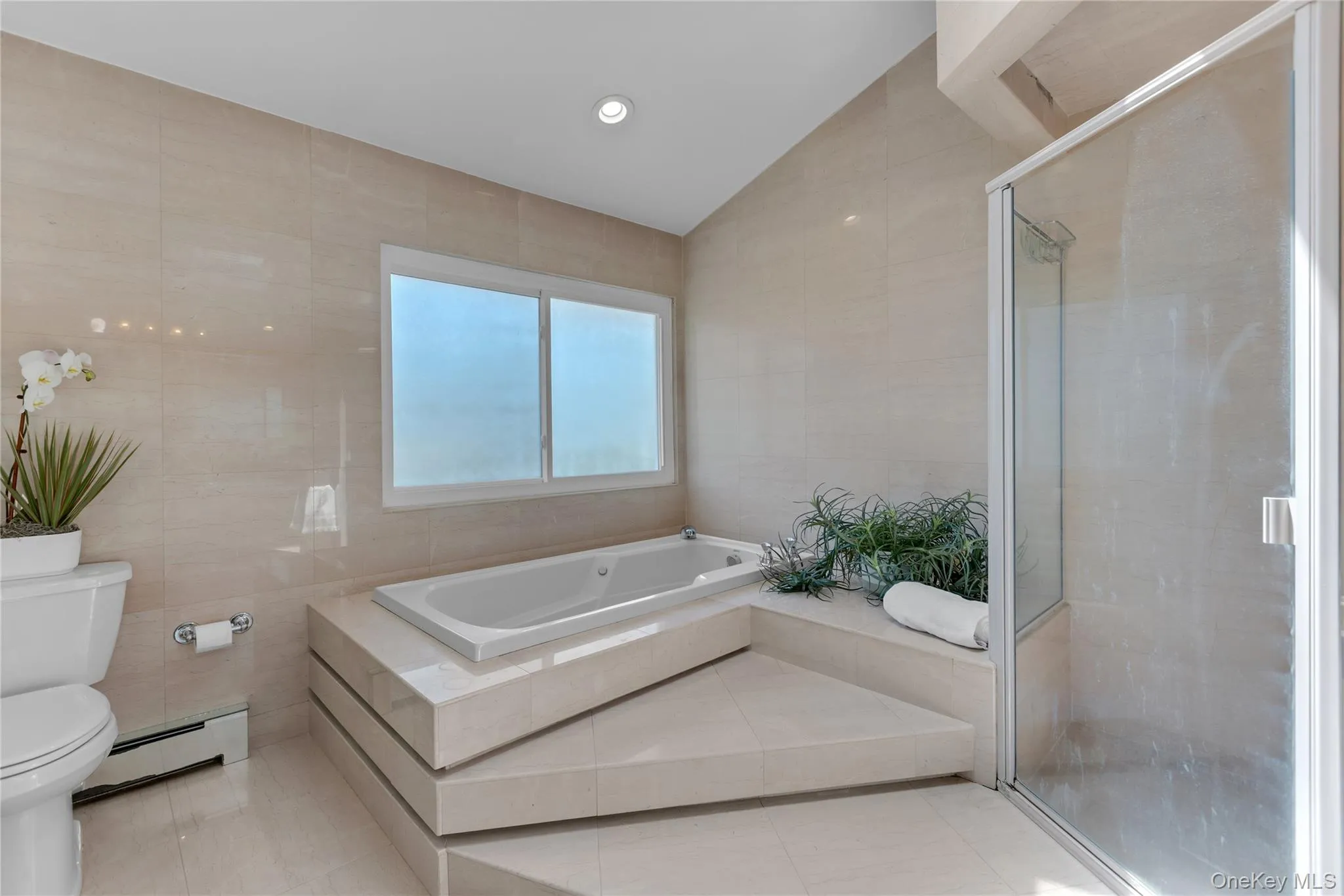 Built-in soaking tub with a tiled surround, frosted windows, and a glass-enclosed shower Built-in soaking tub with a tiled surround, frosted windows, and a glass-enclosed shower