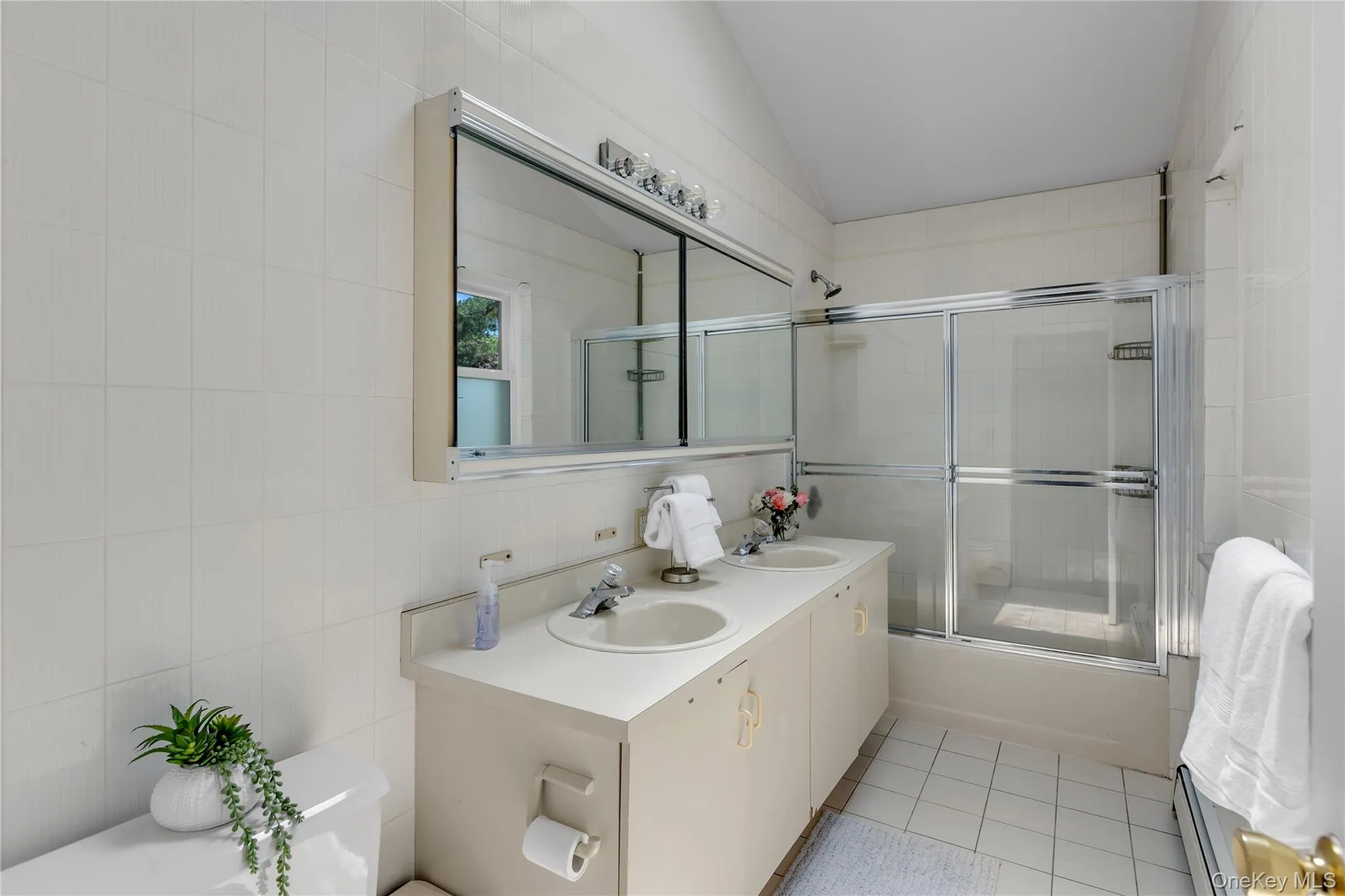 Bathroom featuring a dual-basin vanity with integrated sinks, a mirrored medicine cabinet, and a shower-bathtub combination with sliding glass doors Bathroom featuring a dual-basin vanity with integrated sinks, a mirrored medicine cabinet, and a shower-bathtub combination with sliding glass doors