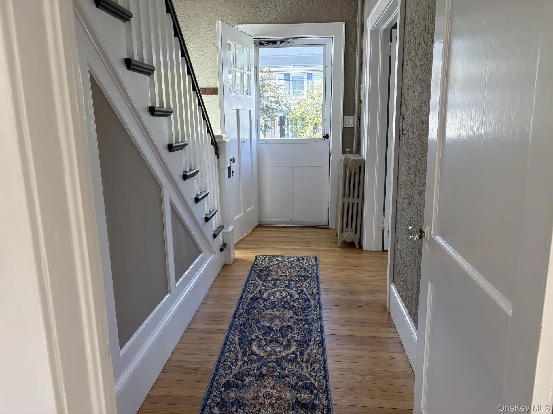Hardwood flooring, painted staircase with dark treads, white paneling, white interior doors, and a radiator Hardwood flooring, painted staircase with dark treads, white paneling, white interior doors, and a radiator