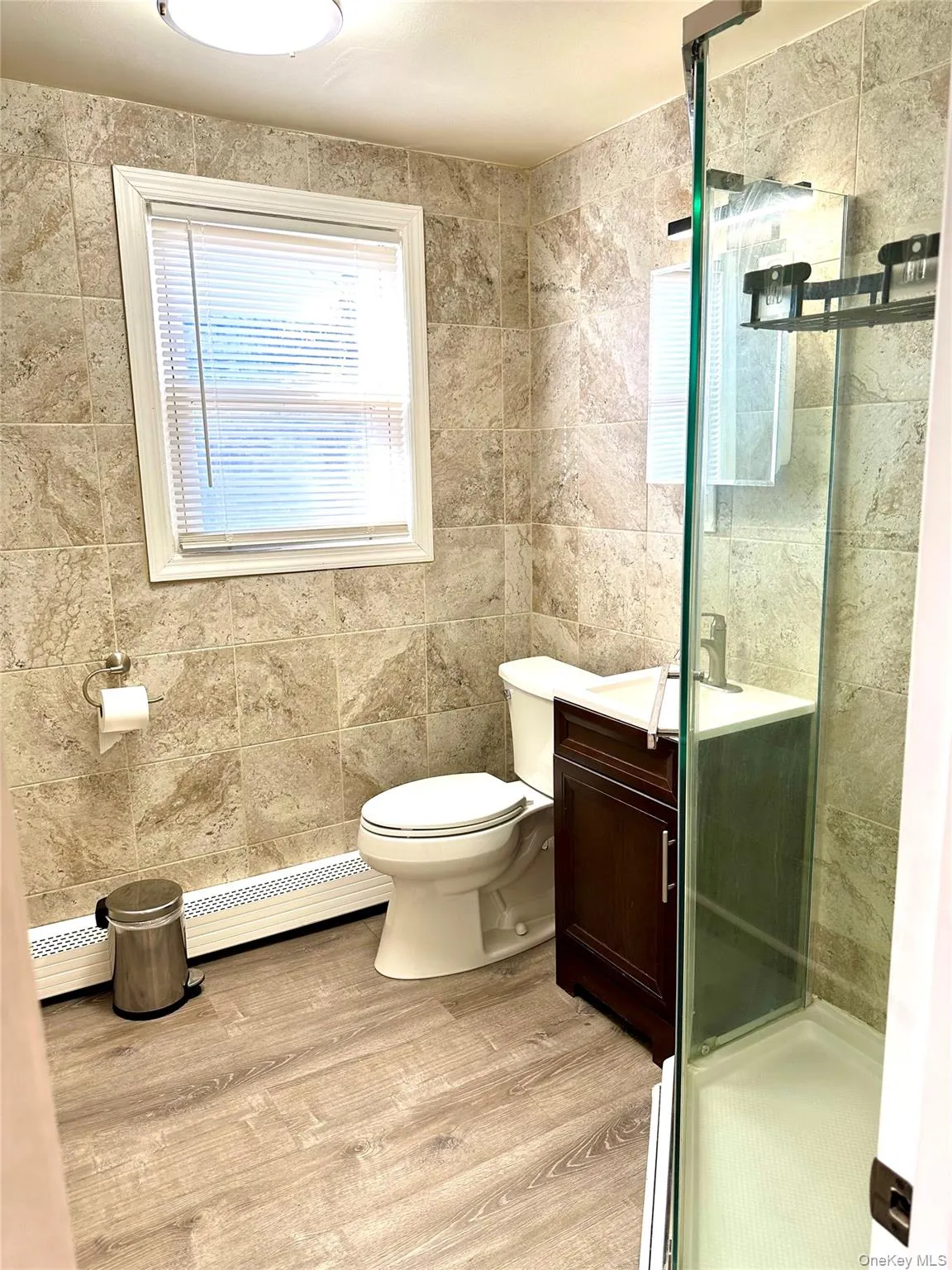 Bathroom featuring a baseboard radiator, hardwood / wood-style flooring, vanity, walk in shower, and toilet Bathroom featuring a baseboard radiator, hardwood / wood-style flooring, vanity, walk in shower, and toilet