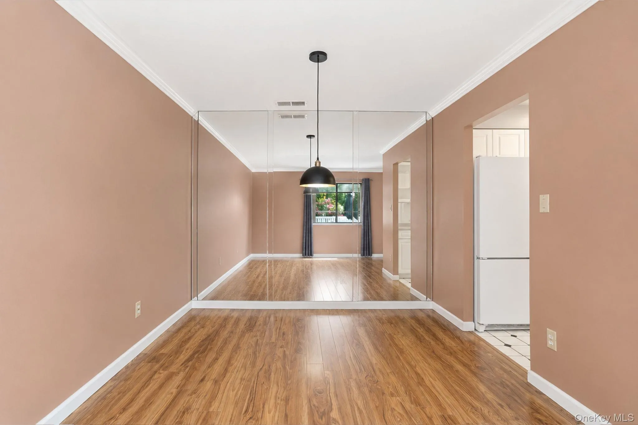 Dining room with laminate wood style flooring featuring a floor to ceiling full wall glass mirror. Dining room with laminate wood style flooring featuring a floor to ceiling full wall glass mirror.