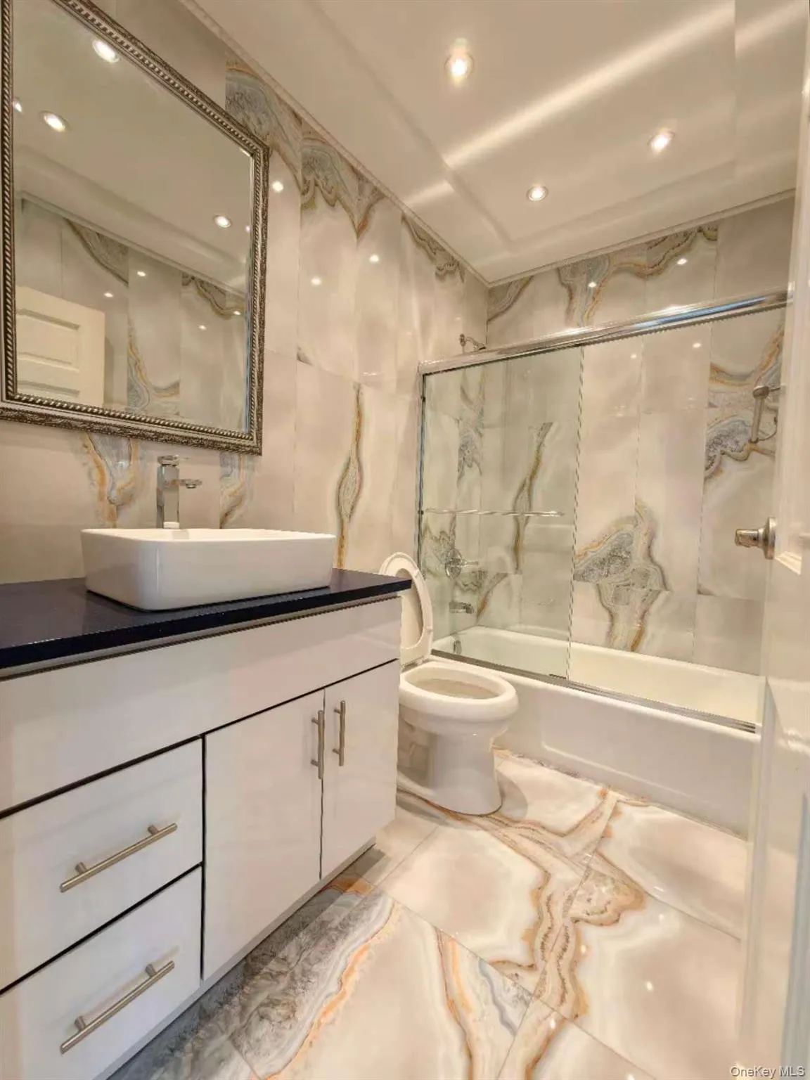 Full bath featuring tile walls, combined bath / shower with glass door, vanity, and recessed lighting Full bath featuring tile walls, combined bath / shower with glass door, vanity, and recessed lighting