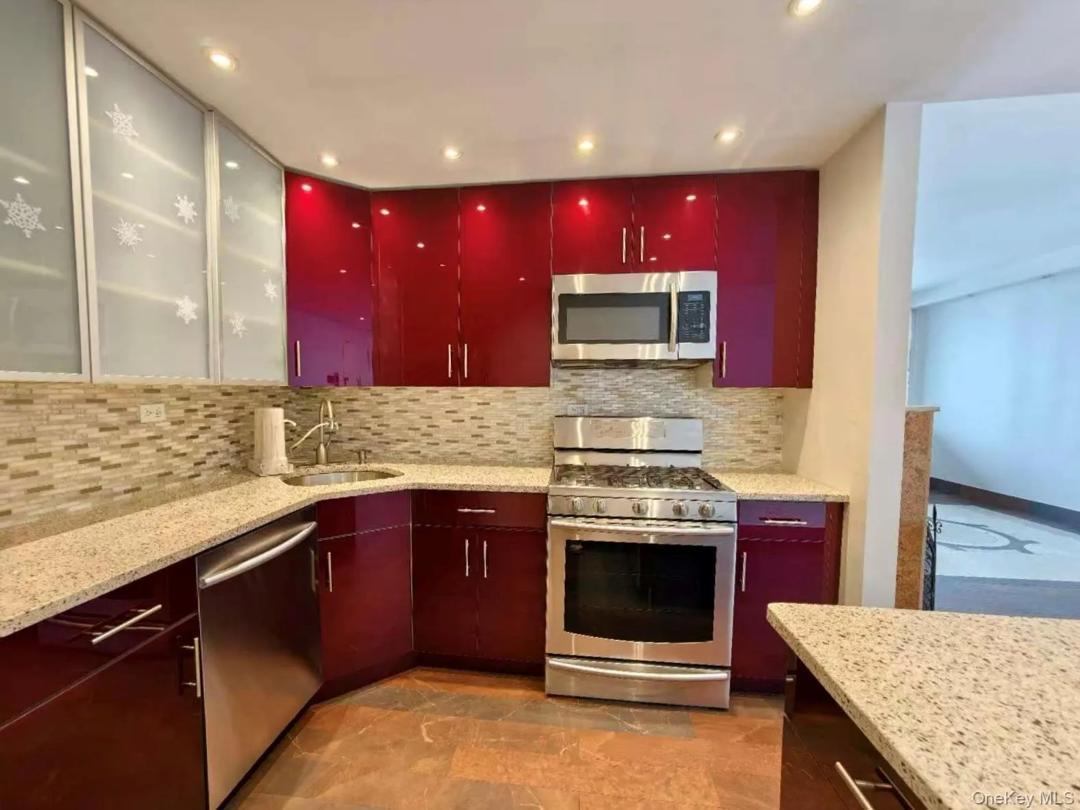 Kitchen featuring appliances with stainless steel finishes, red cabinetry, backsplash, recessed lighting, and light stone countertops Kitchen featuring appliances with stainless steel finishes, red cabinetry, backsplash, recessed lighting, and light stone countertops