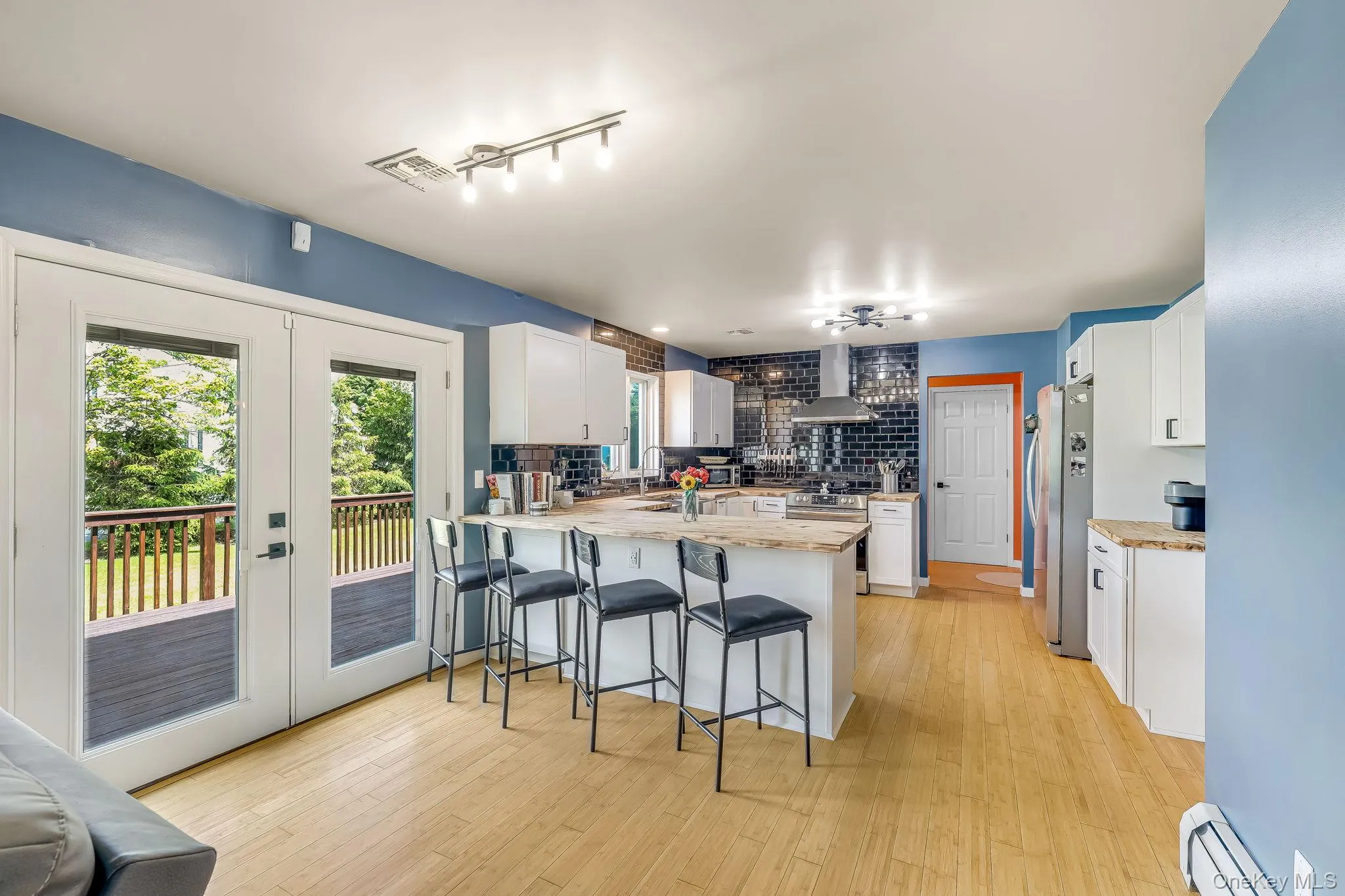 The kitchen boasts an island with seating, white cabinetry, stainless steel appliances, subway tile backsplash, and hardwood flooring. The kitchen boasts an island with seating, white cabinetry, stainless steel appliances, subway tile backsplash, and hardwood flooring.