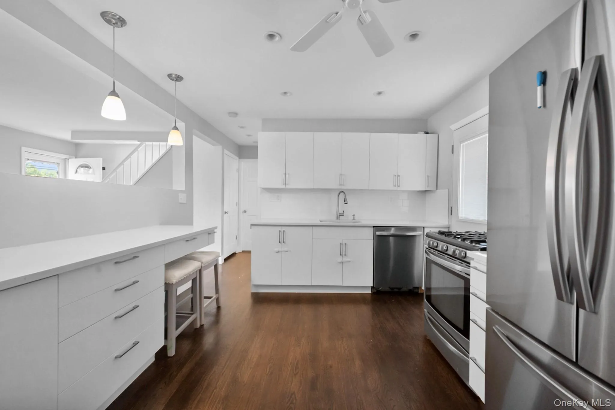 Modern kitchen featuring white cabinetry, stainless steel appliances, wood-finish flooring, recessed lighting, and a peninsula with pendant lights Modern kitchen featuring white cabinetry, stainless steel appliances, wood-finish flooring, recessed lighting, and a peninsula with pendant lights