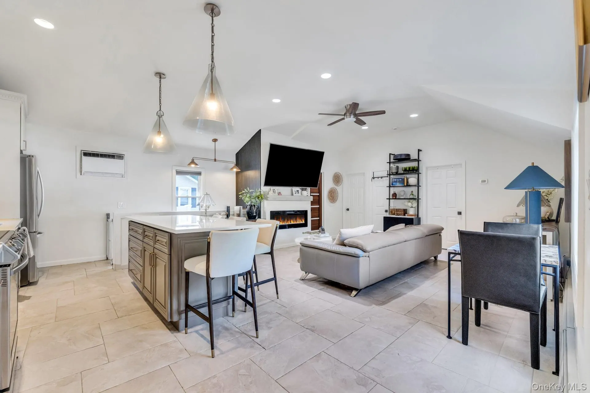 Open-concept living space featuring a kitchen island with seating, stainless steel appliances, tile flooring, a vaulted ceiling, and a built-in fireplace Open-concept living space featuring a kitchen island with seating, stainless steel appliances, tile flooring, a vaulted ceiling, and a built-in fireplace