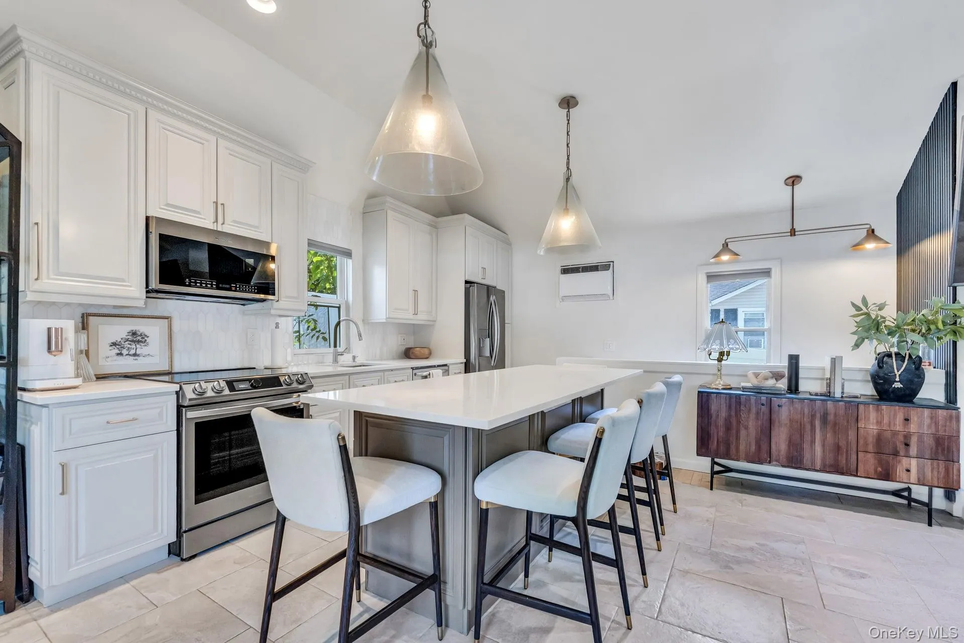 Bright kitchen featuring an expansive center island with seating, white shaker cabinetry, stainless steel appliances, and a tiled backsplash Bright kitchen featuring an expansive center island with seating, white shaker cabinetry, stainless steel appliances, and a tiled backsplash