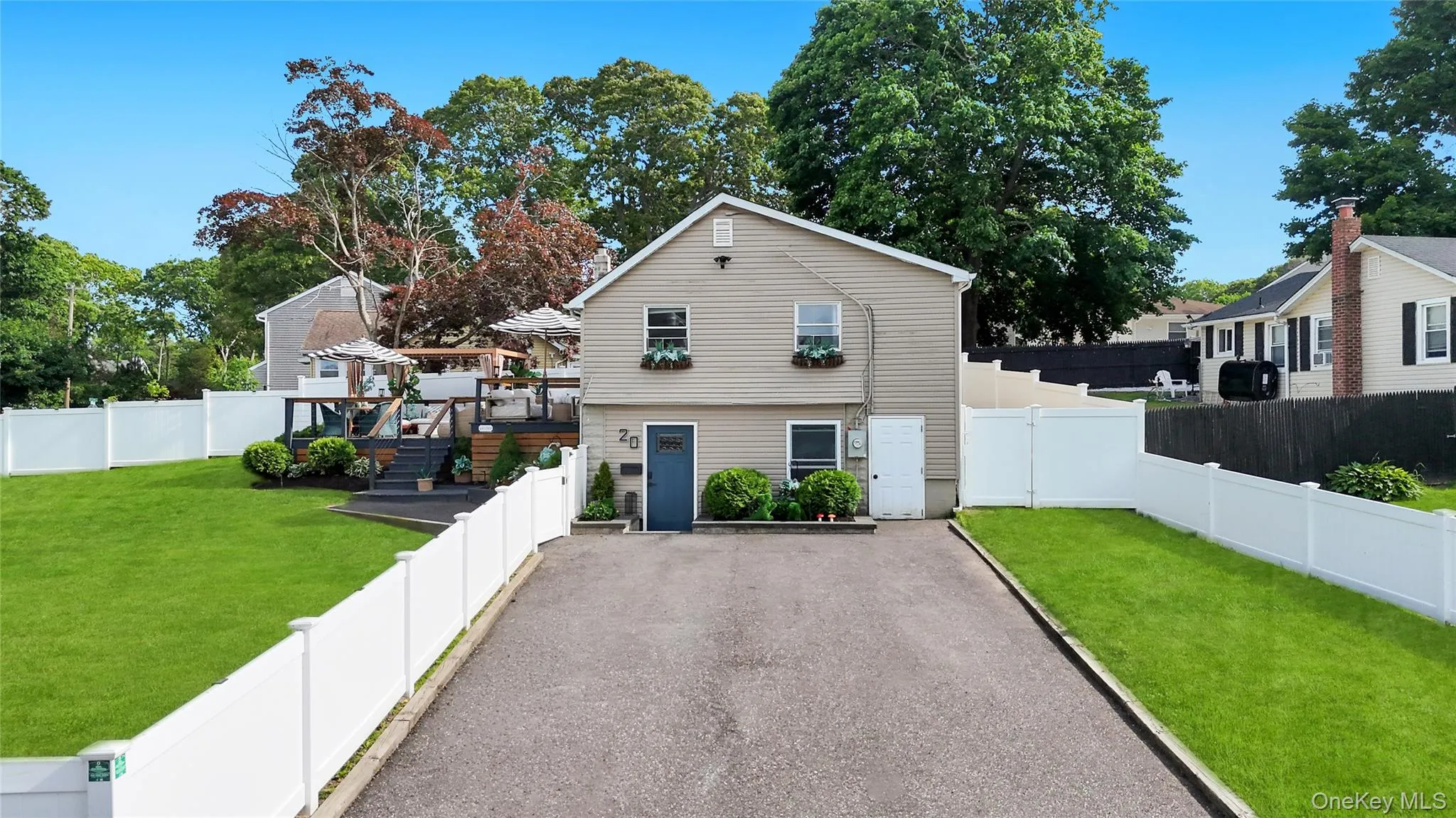 Vinyl-sided residence featuring a multi-level rear deck, a paved driveway, and white privacy fencing Vinyl-sided residence featuring a multi-level rear deck, a paved driveway, and white privacy fencing