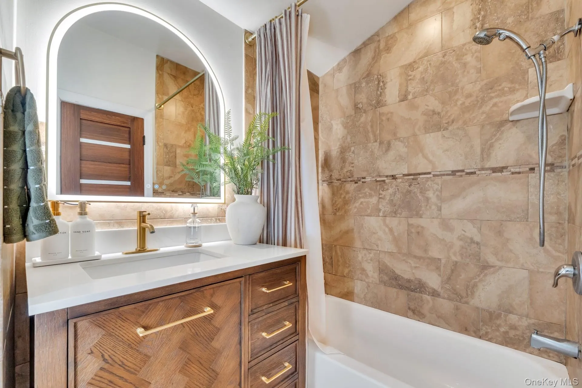 Bathroom featuring a white bathtub, tiled shower surround with decorative accent band, and a vanity with a white countertop Bathroom featuring a white bathtub, tiled shower surround with decorative accent band, and a vanity with a white countertop