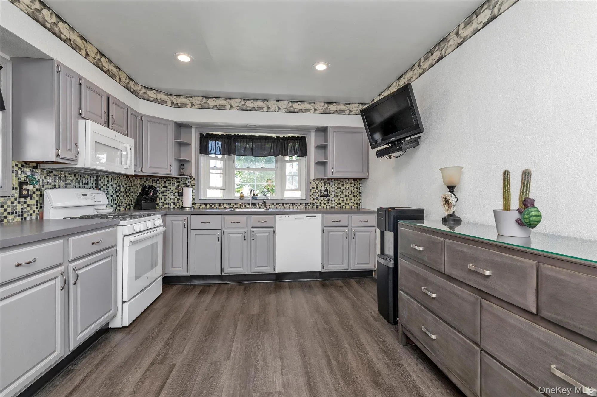 Kitchen featuring updated cabinetry, wood-finish flooring, white appliances, a mosaic tile backsplash with recessed lighting. Kitchen featuring updated cabinetry, wood-finish flooring, white appliances, a mosaic tile backsplash with recessed lighting.