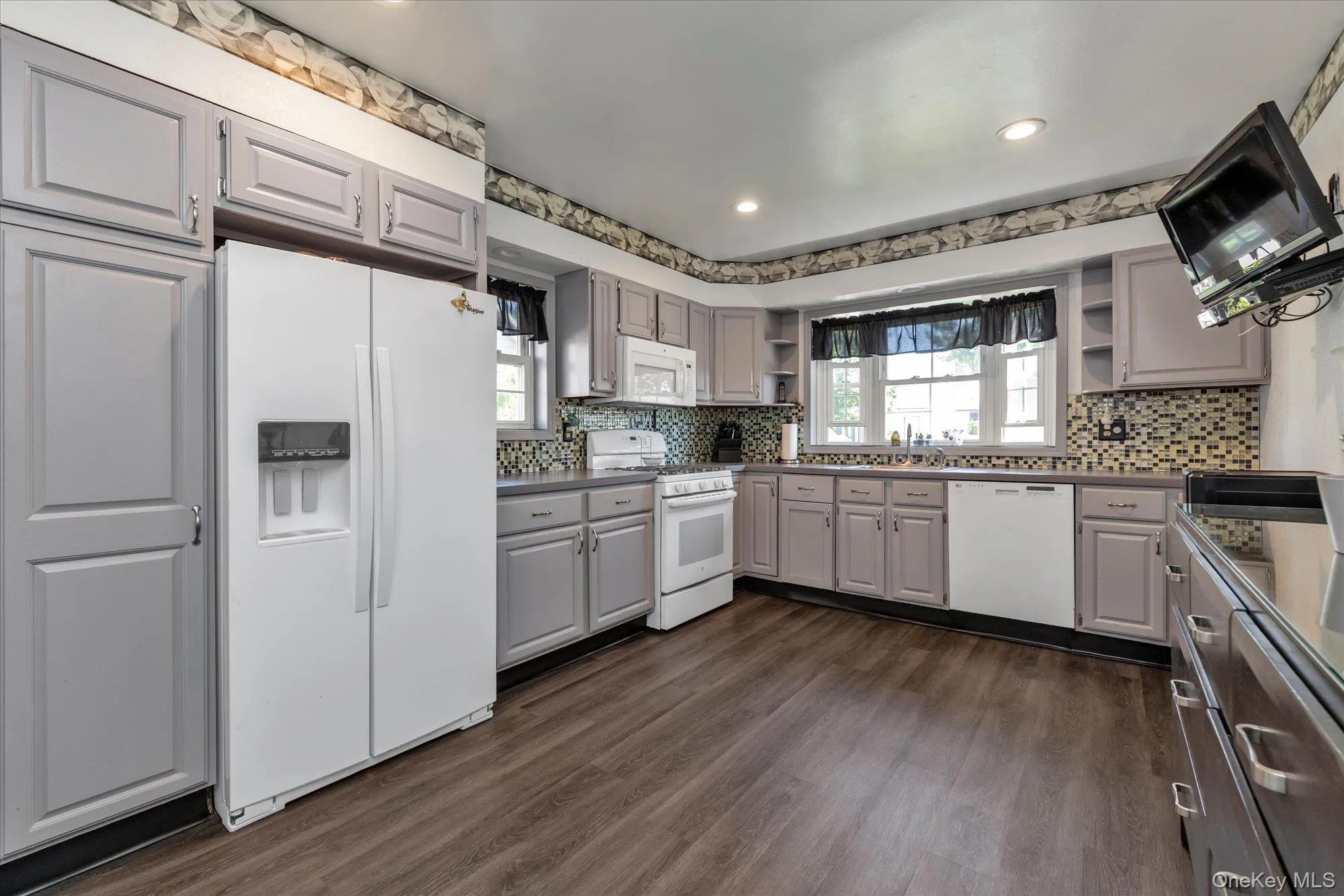 Kitchen featuring updated cabinetry, wood-finish flooring, white appliances, a mosaic tile backsplash with recessed lighting. Kitchen featuring updated cabinetry, wood-finish flooring, white appliances, a mosaic tile backsplash with recessed lighting.