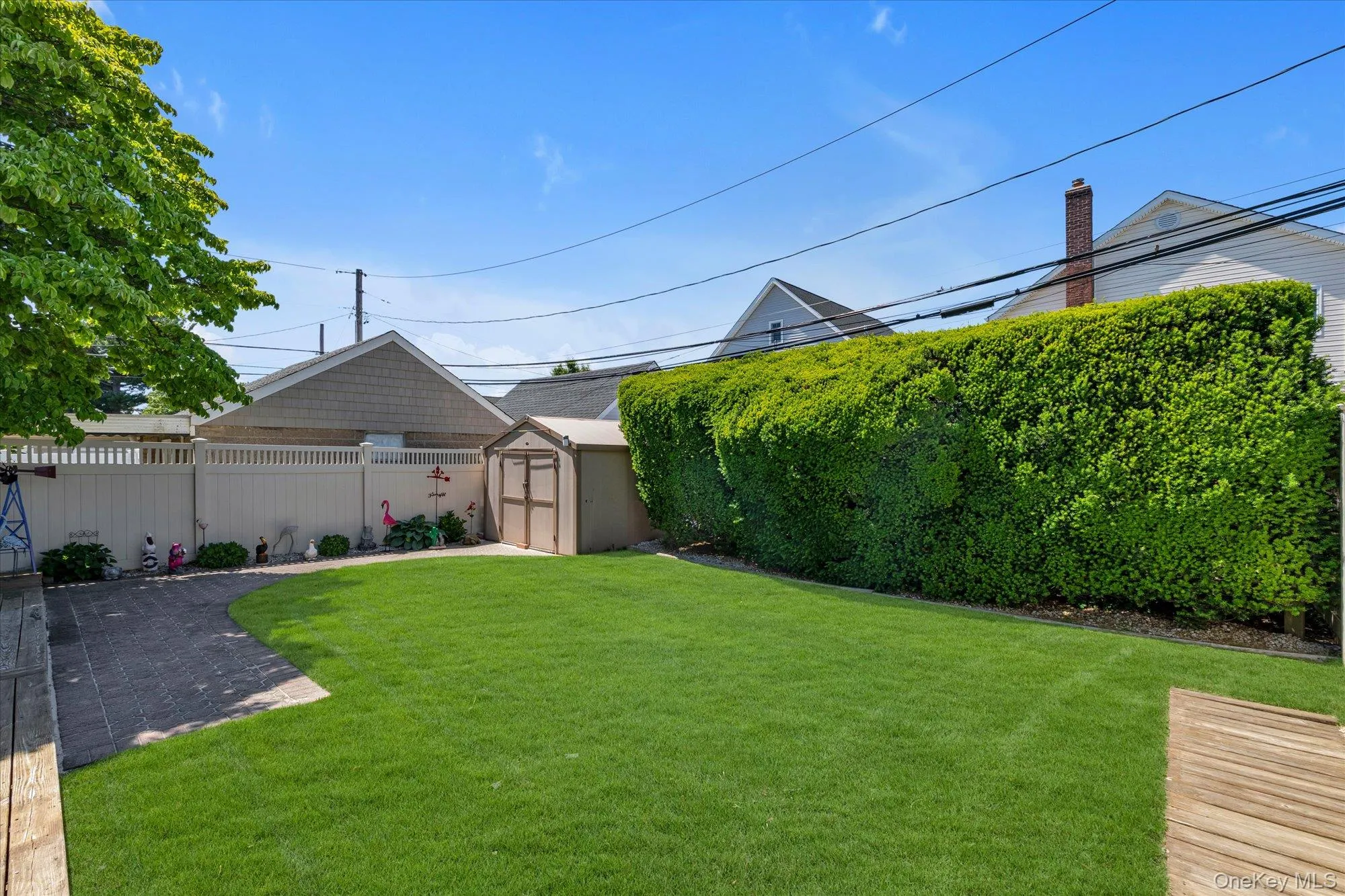Expansive backyard featuring a lush lawn, mature perimeter hedging, a dedicated patio space, and a storage shed. Expansive backyard featuring a lush lawn, mature perimeter hedging, a dedicated patio space, and a storage shed.
