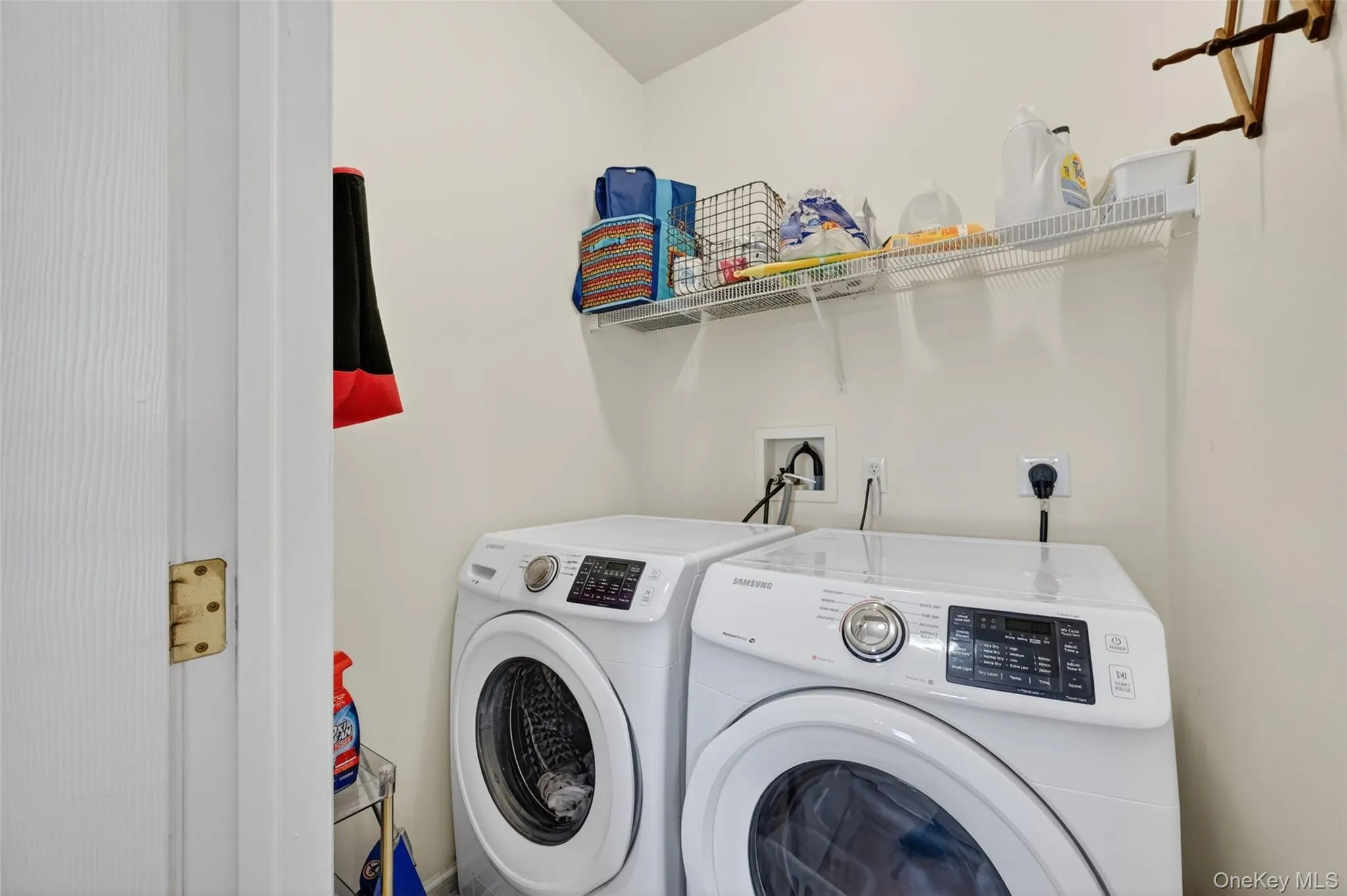 Laundry area with a wire shelf, light-colored walls, and a front-loading washer and dryer Laundry area with a wire shelf, light-colored walls, and a front-loading washer and dryer