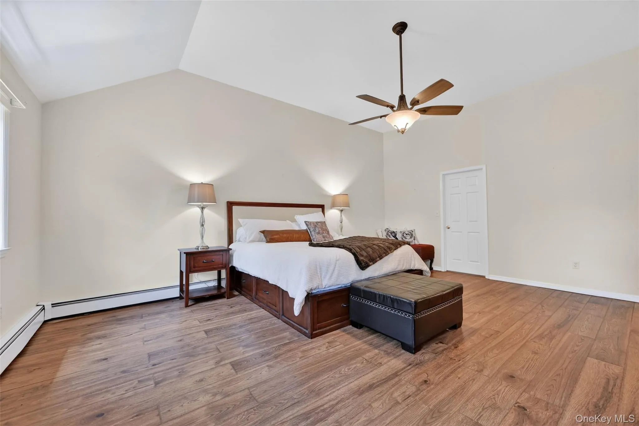 Vaulted ceiling bedroom featuring wood-finish flooring, a ceiling fan with integrated lighting, and a white paneled door Vaulted ceiling bedroom featuring wood-finish flooring, a ceiling fan with integrated lighting, and a white paneled door