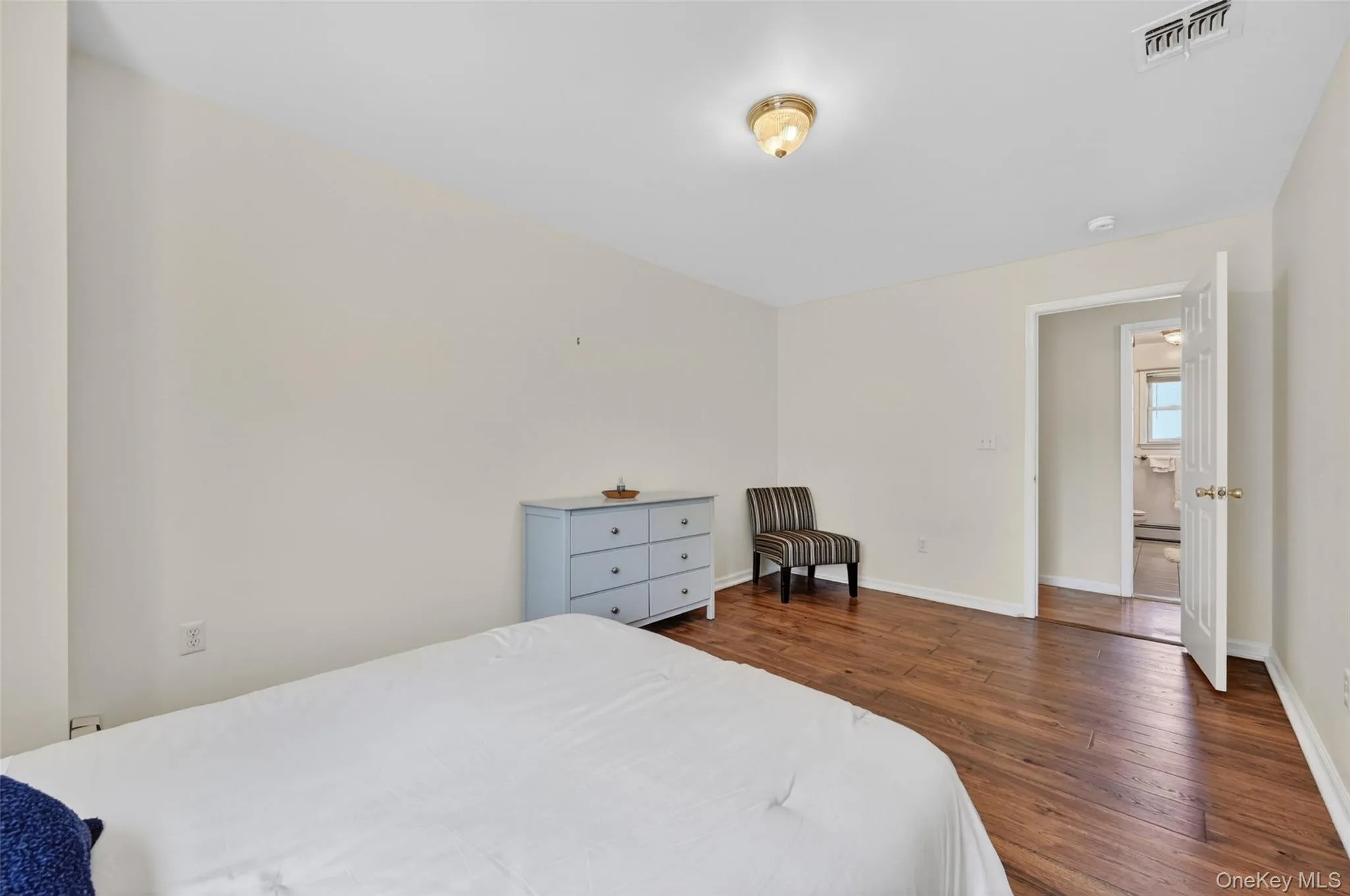 Spacious room featuring wood-finish flooring, light-toned walls, and a ceiling-mounted light fixture Spacious room featuring wood-finish flooring, light-toned walls, and a ceiling-mounted light fixture