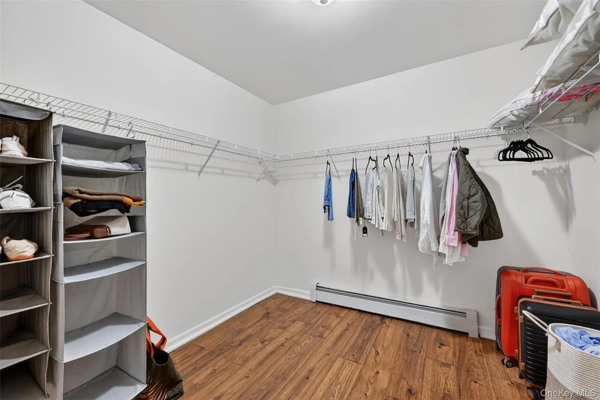 Spacious walk-in closet featuring wire shelving, wire hanging rods, and wood-finish flooring Spacious walk-in closet featuring wire shelving, wire hanging rods, and wood-finish flooring