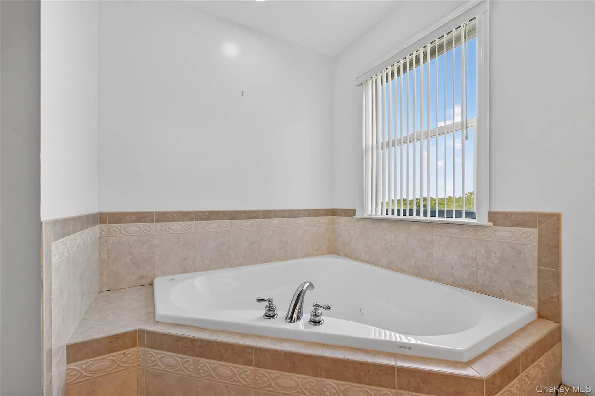 Corner soaking tub with polished chrome fixtures, surrounded by a tile deck and wainscoting Corner soaking tub with polished chrome fixtures, surrounded by a tile deck and wainscoting