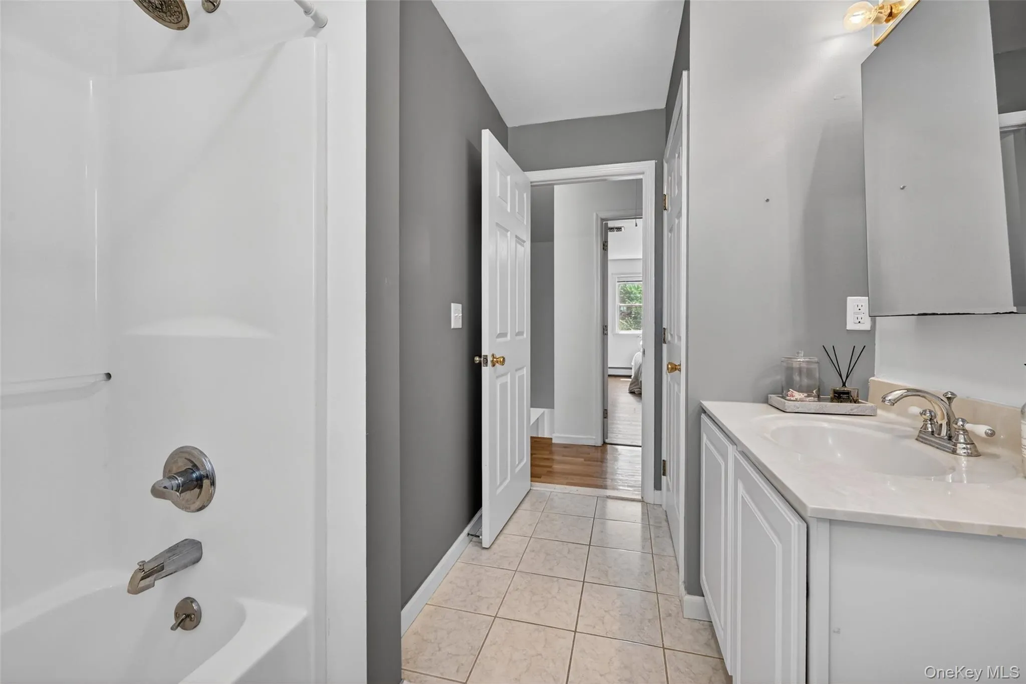 Bathroom featuring a shower/tub combination with chrome fixtures, a single vanity with white cabinetry and a light-toned countertop, and neutral-toned tiled flooring Bathroom featuring a shower/tub combination with chrome fixtures, a single vanity with white cabinetry and a light-toned countertop, and neutral-toned tiled flooring