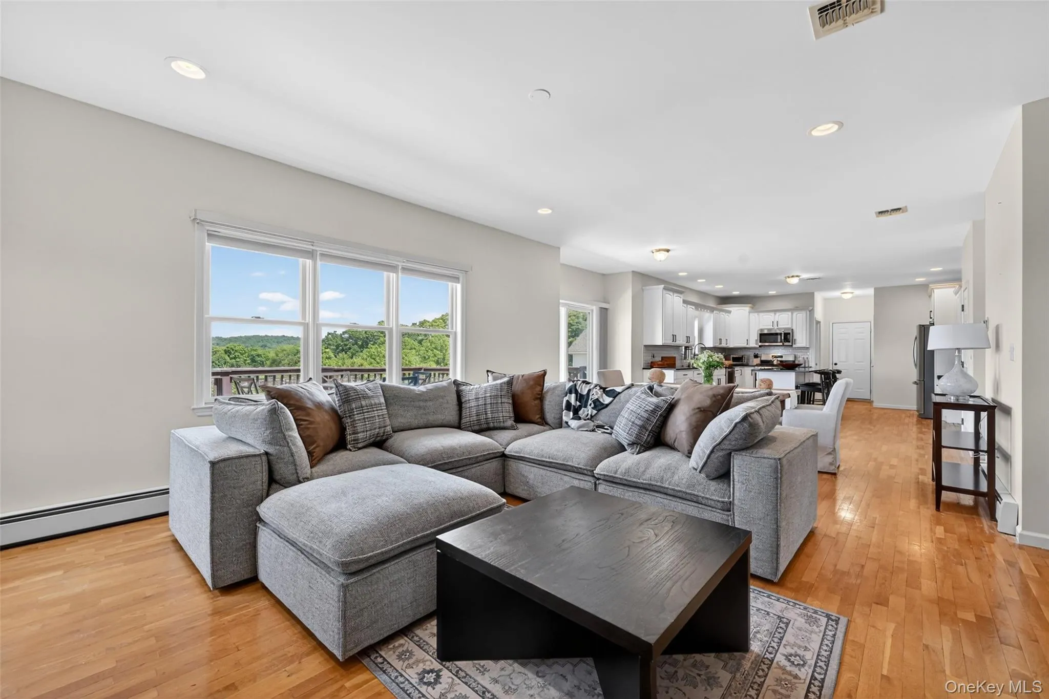 Bright living area featuring wood-finish flooring, recessed lighting, and a triple window offering outdoor scenery Bright living area featuring wood-finish flooring, recessed lighting, and a triple window offering outdoor scenery