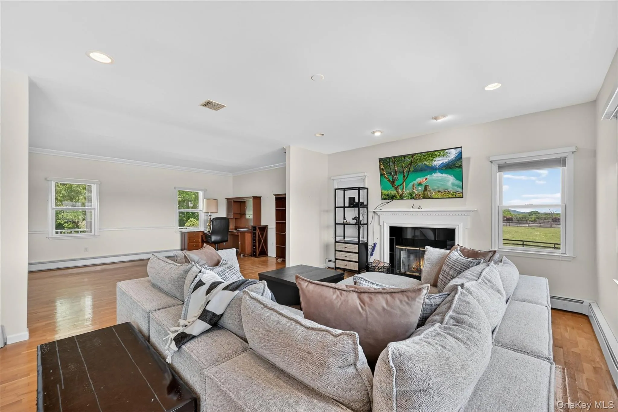 Living area featuring a fireplace with a white mantel, recessed lighting, wood-finish flooring, and multiple windows Living area featuring a fireplace with a white mantel, recessed lighting, wood-finish flooring, and multiple windows