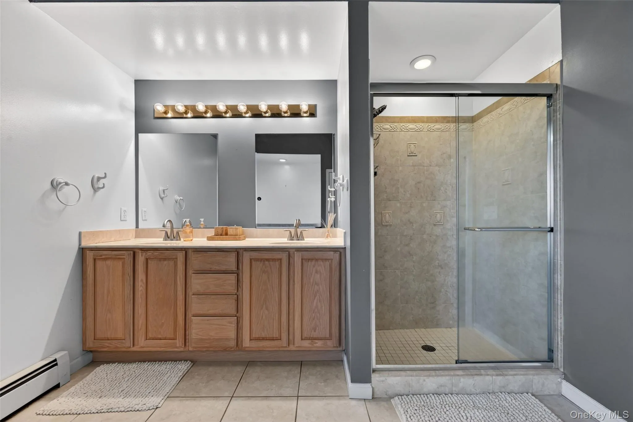 Double vanity with wood cabinetry and dual mirrors, complemented by a large glass-enclosed shower featuring tile surround and recessed lighting Double vanity with wood cabinetry and dual mirrors, complemented by a large glass-enclosed shower featuring tile surround and recessed lighting