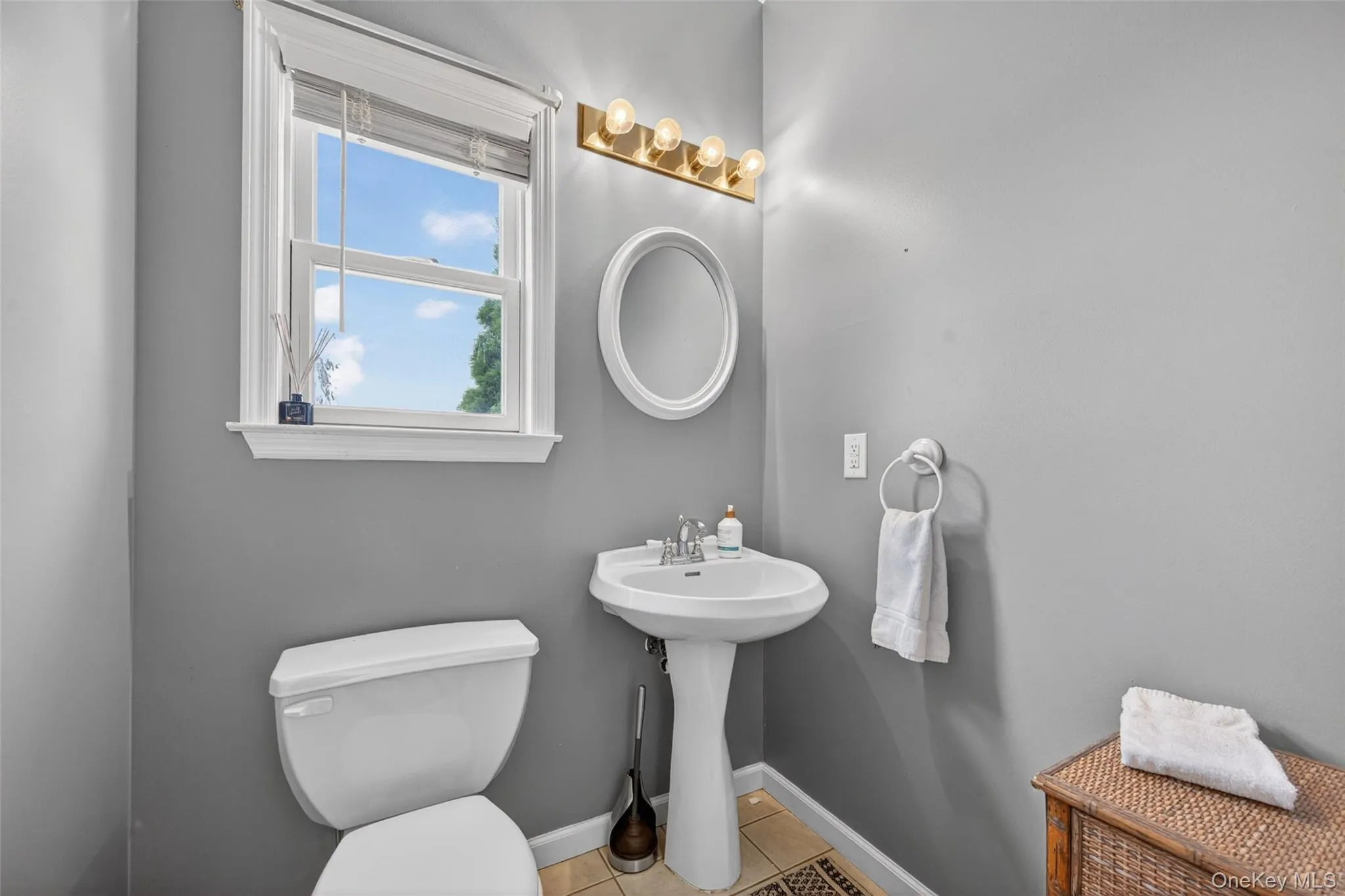 Well-lit Down stairs bathroom featuring a pedestal sink, toilet, and window with a white frame Well-lit Down stairs bathroom featuring a pedestal sink, toilet, and window with a white frame