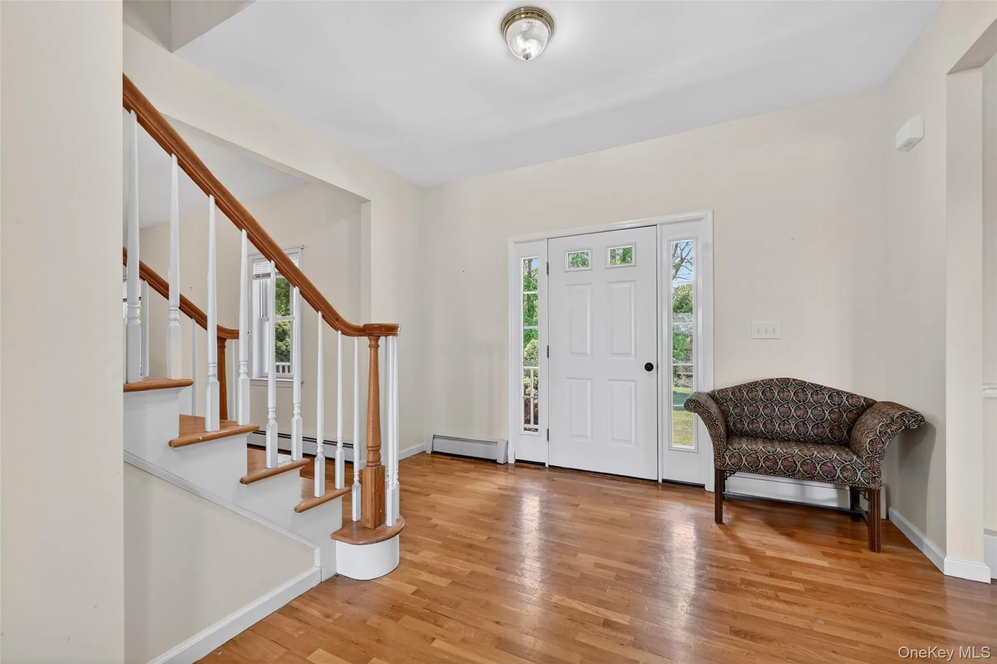 Front entryway featuring wood-finish flooring, a white paneled door with sidelight windows, and a staircase with a wood handrail and white balusters Front entryway featuring wood-finish flooring, a white paneled door with sidelight windows, and a staircase with a wood handrail and white balusters