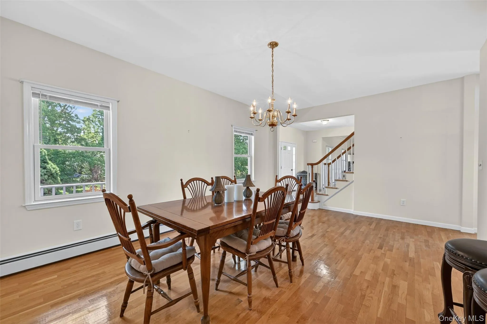 Spacious dining area featuring wood-finish flooring, two windows, and a brass chandelier Spacious dining area featuring wood-finish flooring, two windows, and a brass chandelier