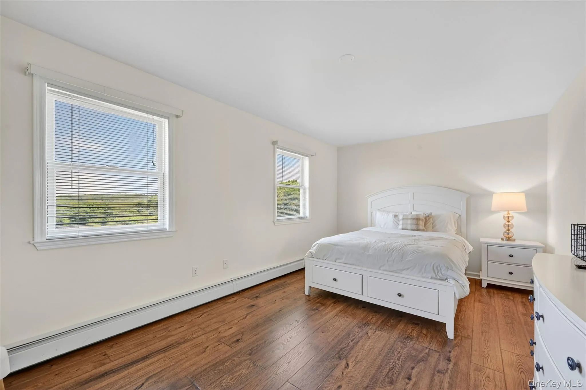 Bedroom featuring durable wood-finish flooring, two window openings, neutral wall paint, and white trim Bedroom featuring durable wood-finish flooring, two window openings, neutral wall paint, and white trim