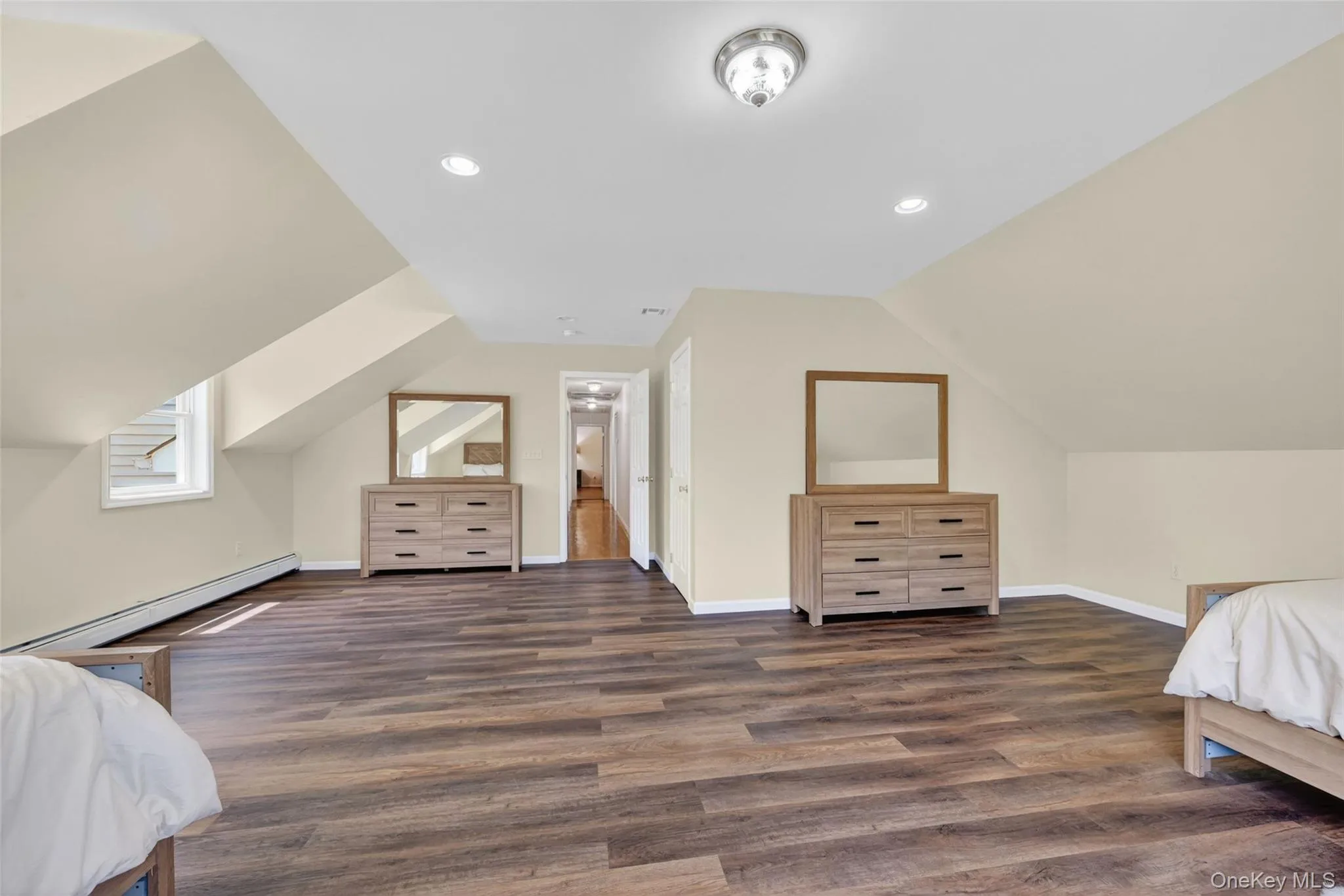 Spacious room featuring sloped ceilings, recessed lighting, wood-finish flooring, and light-colored wall paint Spacious room featuring sloped ceilings, recessed lighting, wood-finish flooring, and light-colored wall paint