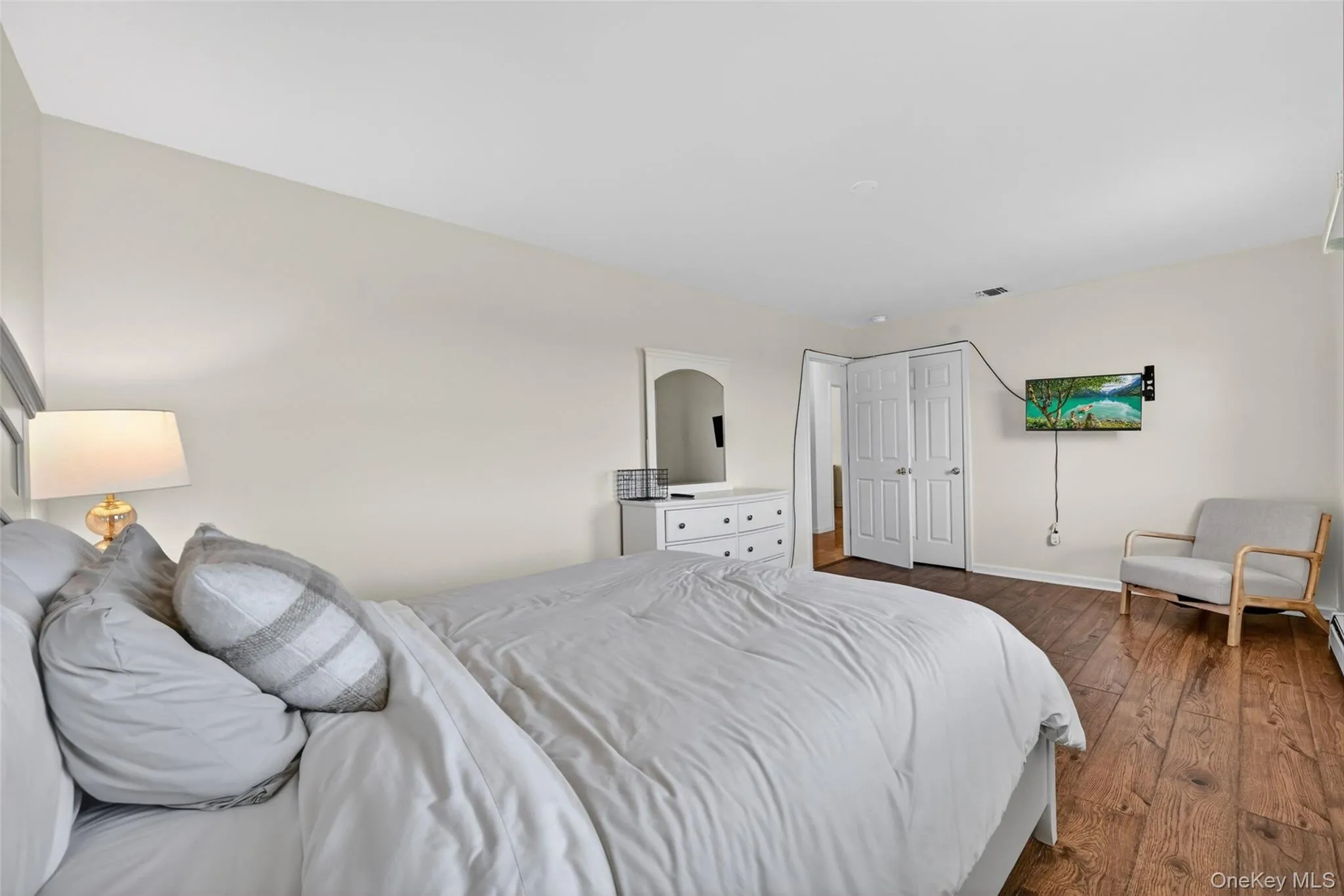 Bedroom featuring wood-finish flooring, neutral wall tones, and white bi-fold closet doors Bedroom featuring wood-finish flooring, neutral wall tones, and white bi-fold closet doors
