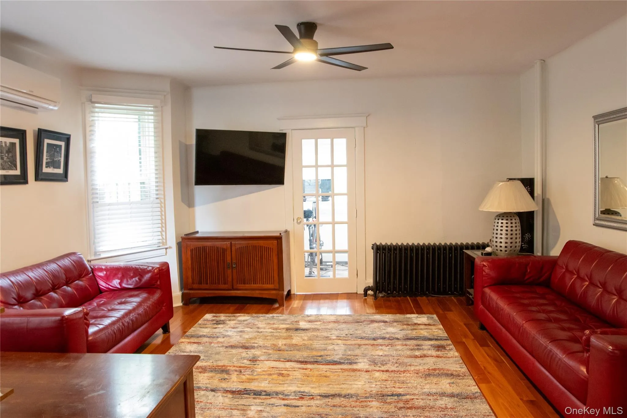 Open-concept living space with wood-finish flooring, a ceiling fan, and white walls Open-concept living space with wood-finish flooring, a ceiling fan, and white walls