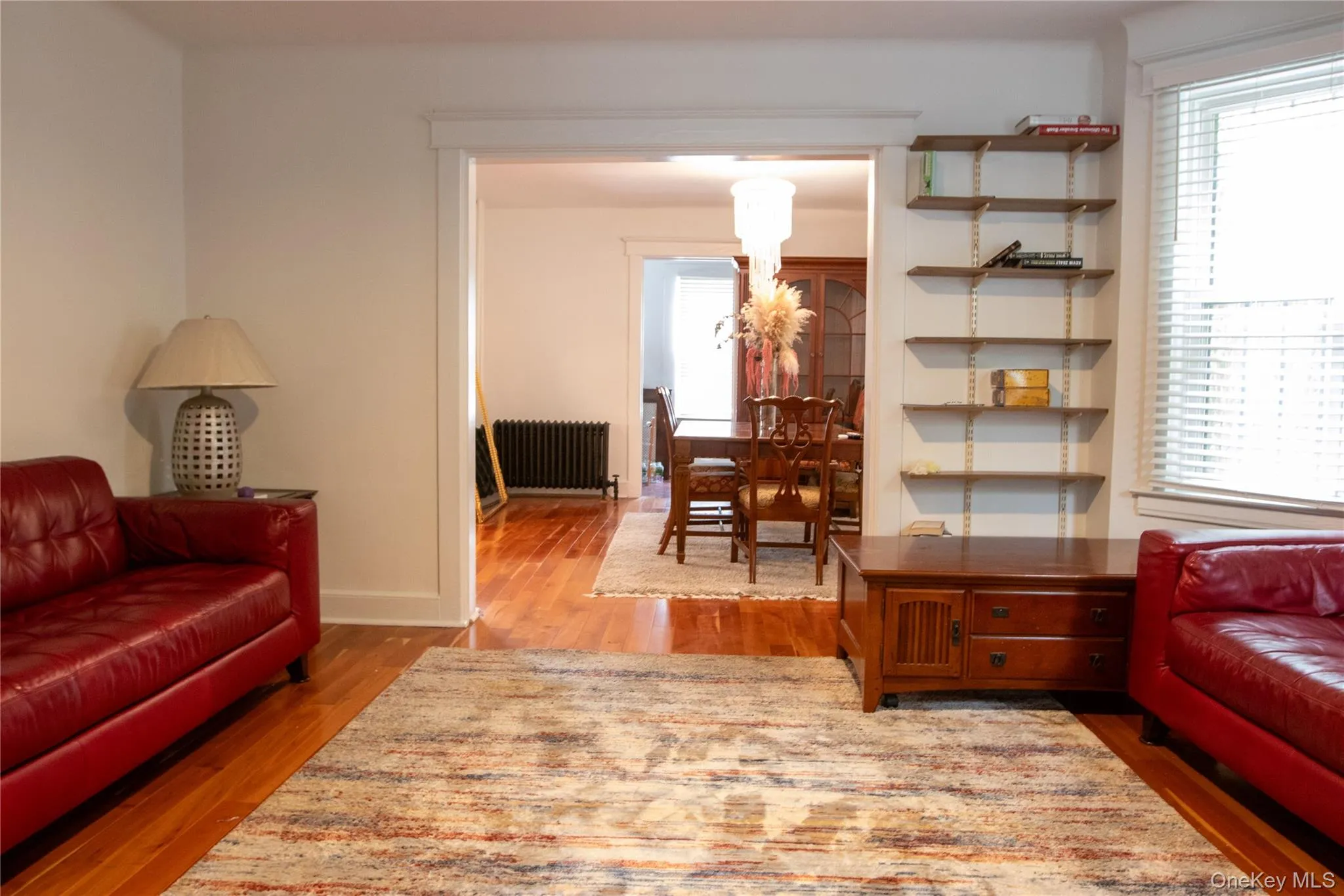 Living area featuring wood-finish flooring, a wide entry to an additional room, and a built-in shelving system Living area featuring wood-finish flooring, a wide entry to an additional room, and a built-in shelving system