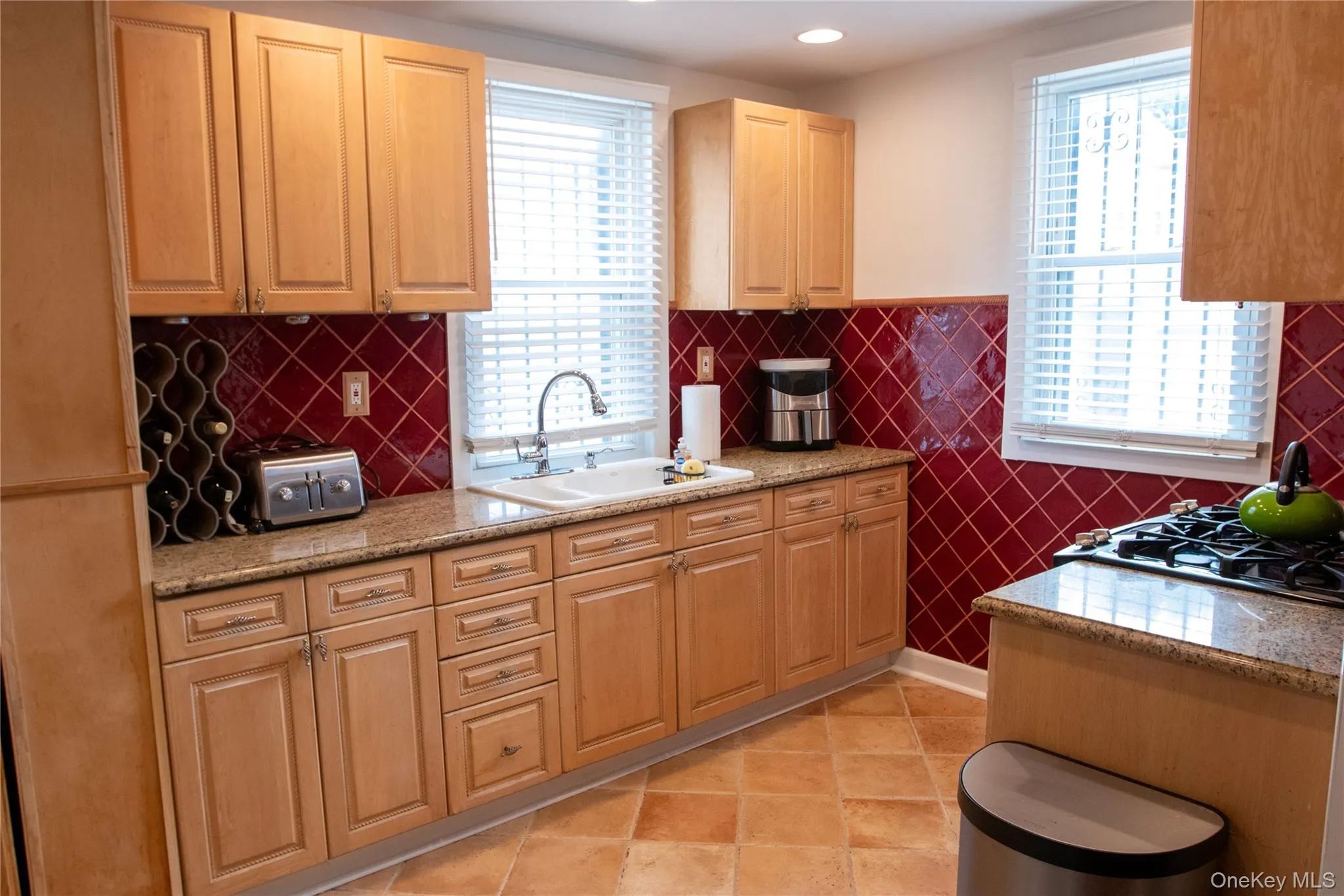 Kitchen featuring wood cabinetry, granite-finish countertops, and a red tiled backsplash Kitchen featuring wood cabinetry, granite-finish countertops, and a red tiled backsplash