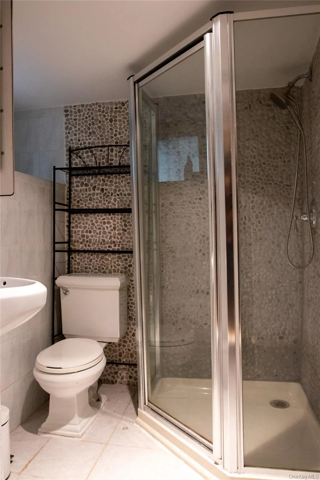 Enclosed corner shower with glass surround, pebble tile shower walls, and a multi-setting showerhead Enclosed corner shower with glass surround, pebble tile shower walls, and a multi-setting showerhead