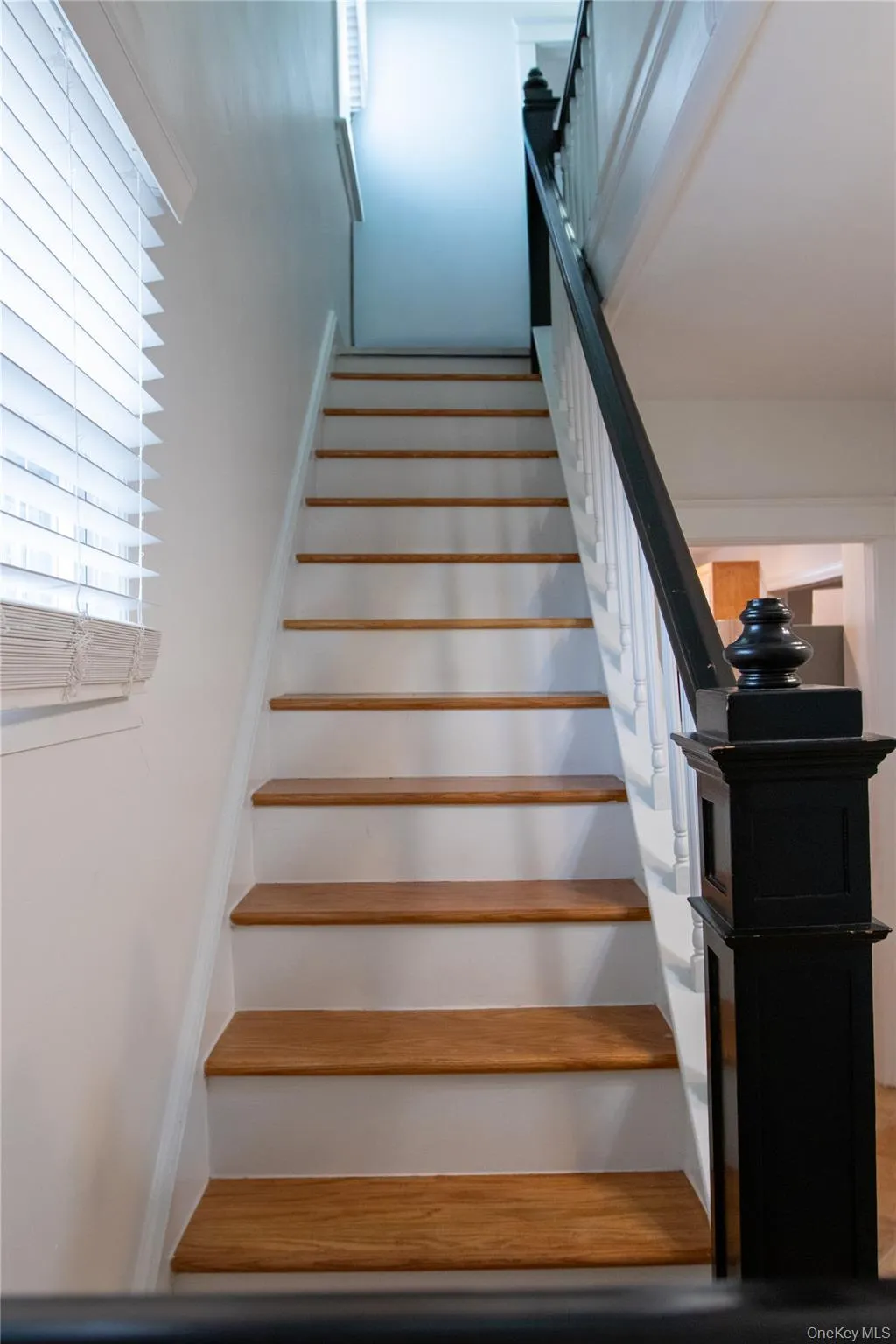 Staircase featuring wood-finish treads, white risers, and a contrasting black newel post with a white spindle railing Staircase featuring wood-finish treads, white risers, and a contrasting black newel post with a white spindle railing