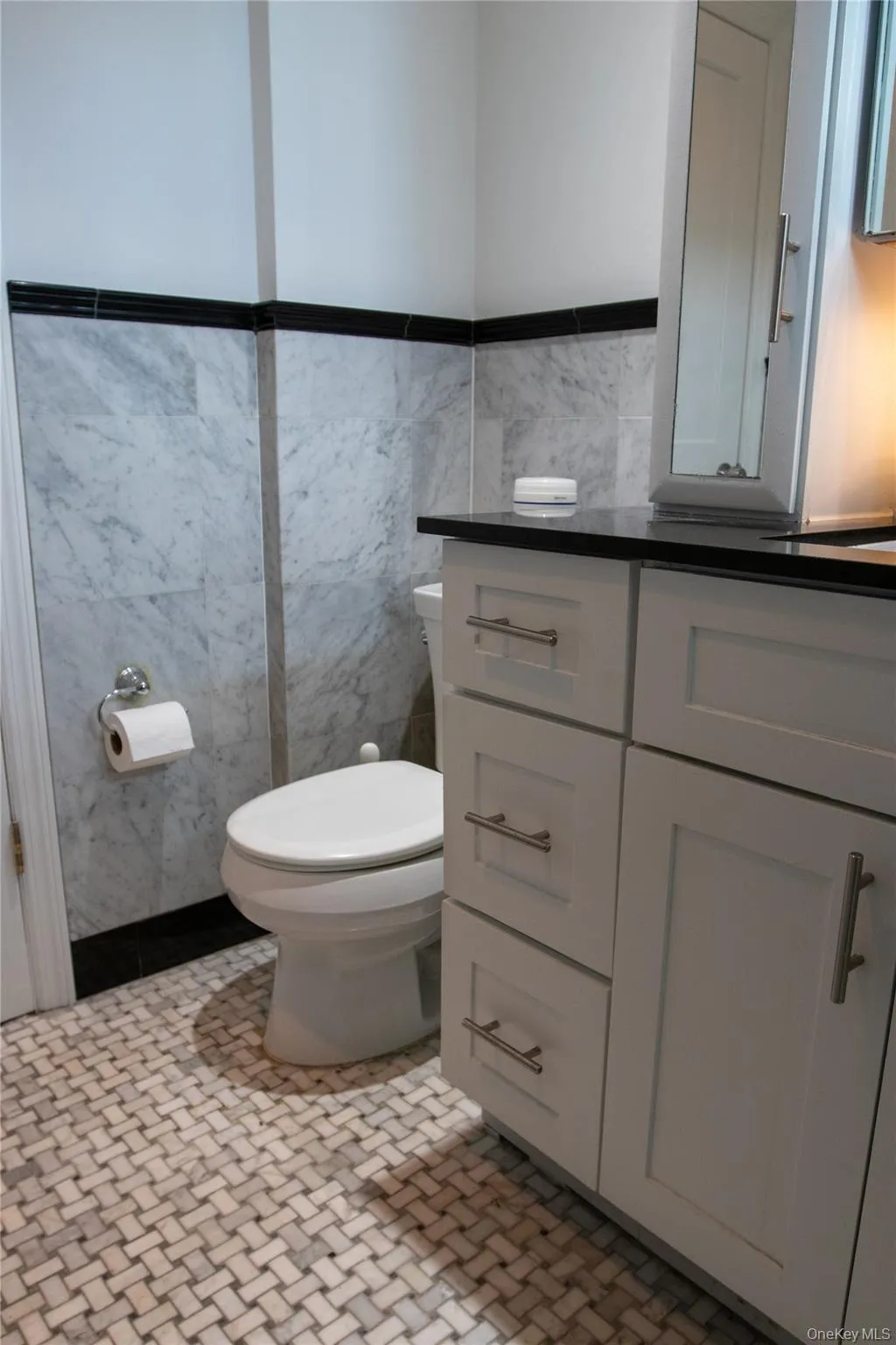 Bathroom featuring a white vanity with brushed nickel hardware, dark countertop, and integrated sink Bathroom featuring a white vanity with brushed nickel hardware, dark countertop, and integrated sink