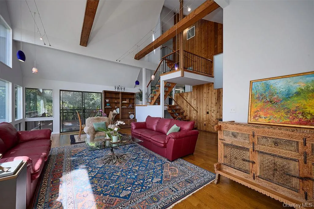 Spacious living area featuring a vaulted ceiling with exposed wood beams, hardwood flooring, and abundant natural light from multiple windows Spacious living area featuring a vaulted ceiling with exposed wood beams, hardwood flooring, and abundant natural light from multiple windows