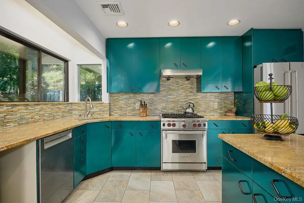 Kitchen featuring teal cabinetry with black hardware, stone tile flooring, and light-toned countertop surfaces Kitchen featuring teal cabinetry with black hardware, stone tile flooring, and light-toned countertop surfaces