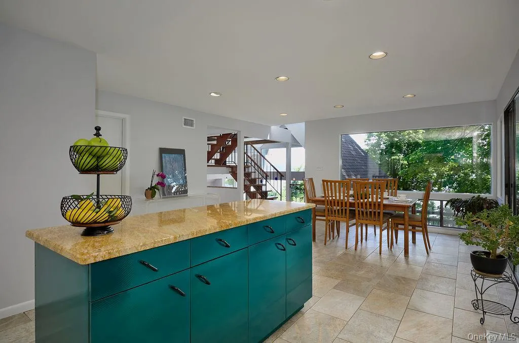 Open-concept living area featuring a kitchen island with stone countertop, recessed lighting, tile flooring, and large windows Open-concept living area featuring a kitchen island with stone countertop, recessed lighting, tile flooring, and large windows