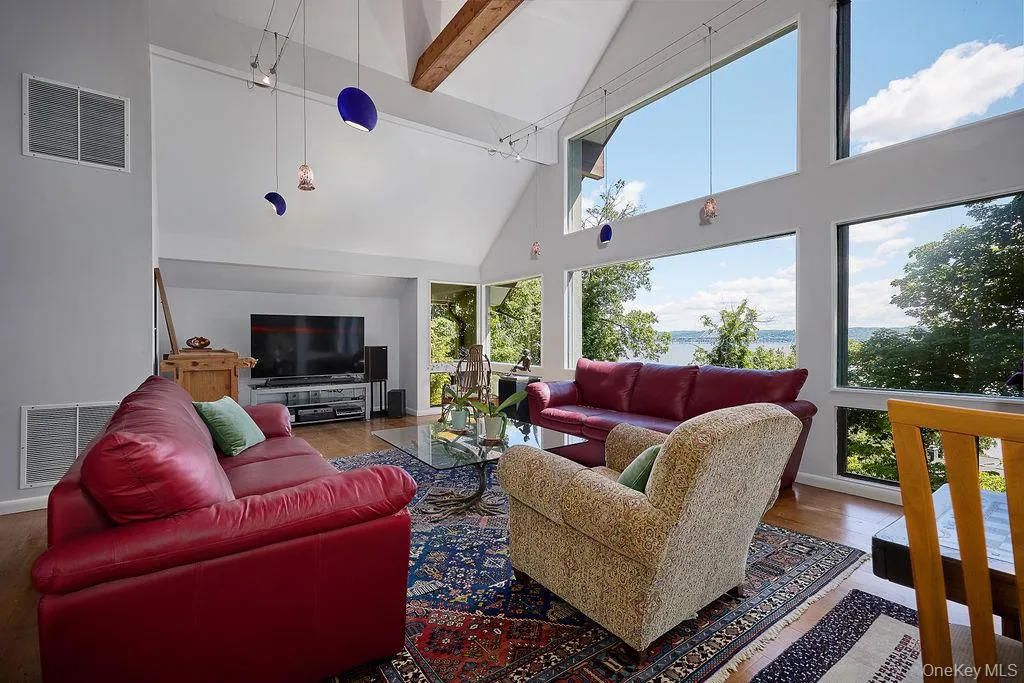 Living area with vaulted ceilings, exposed wood beams, and a wall of windows featuring water scenery Living area with vaulted ceilings, exposed wood beams, and a wall of windows featuring water scenery