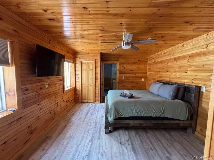 Room featuring wood-plank walls and ceiling, wood-finish flooring, and a ceiling fan Room featuring wood-plank walls and ceiling, wood-finish flooring, and a ceiling fan