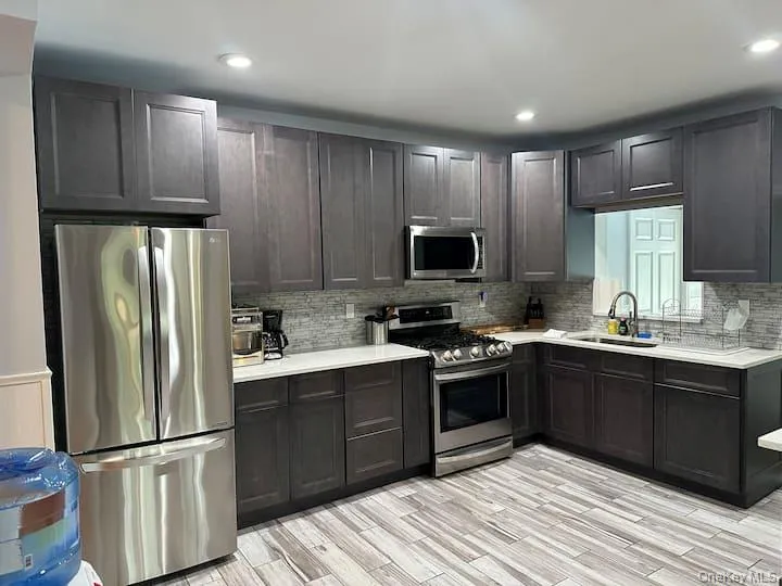 Kitchen featuring dark wood-finish cabinetry, light-toned countertops, a full suite of stainless steel appliances, a tiled backsplash, and recessed lighting Kitchen featuring dark wood-finish cabinetry, light-toned countertops, a full suite of stainless steel appliances, a tiled backsplash, and recessed lighting