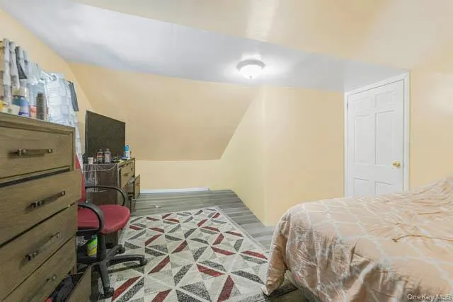 Room with angled ceiling lines, light-toned wall finish, and wood-finish flooring Room with angled ceiling lines, light-toned wall finish, and wood-finish flooring