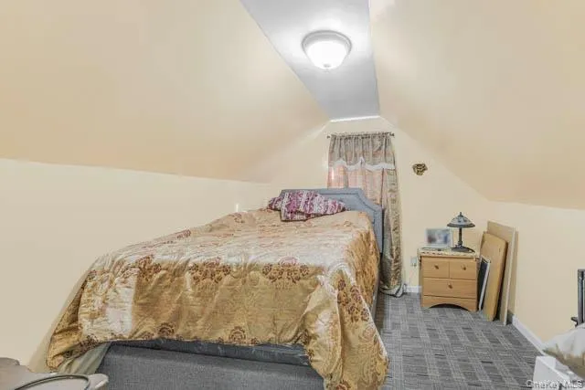 Attic room featuring sloped ceilings, light-colored walls, patterned carpet flooring, and a window with drapes Attic room featuring sloped ceilings, light-colored walls, patterned carpet flooring, and a window with drapes