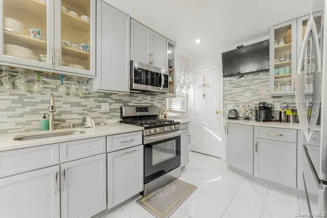 Kitchen featuring light gray cabinetry, stainless steel appliances, a mosaic tile backsplash, and a light-toned countertop Kitchen featuring light gray cabinetry, stainless steel appliances, a mosaic tile backsplash, and a light-toned countertop
