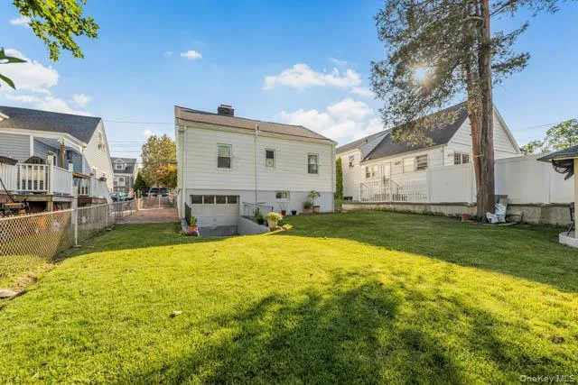 Expansive green lawn with a chain-link fence, mature trees, and a driveway leading to a garage door Expansive green lawn with a chain-link fence, mature trees, and a driveway leading to a garage door
